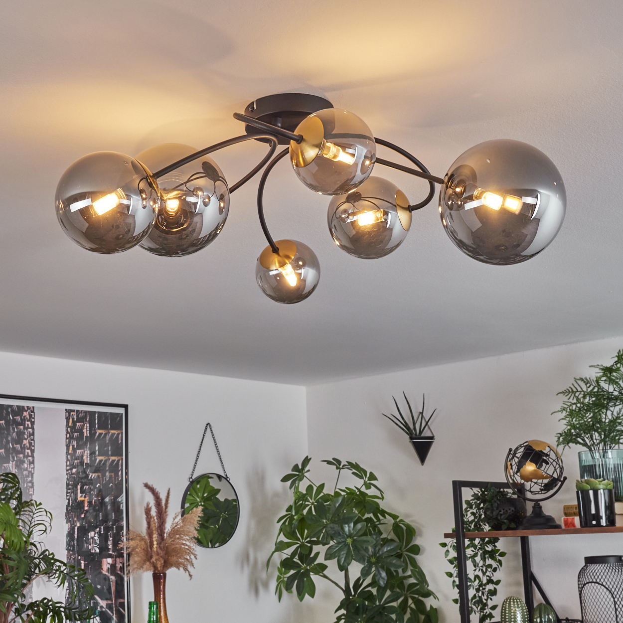 Deckenlampe mit sechs grauen Glaskugeln und schwarzem Rahmen. Im Hintergrund Pflanzen, Spiegel und Regal mit Dekorationen.