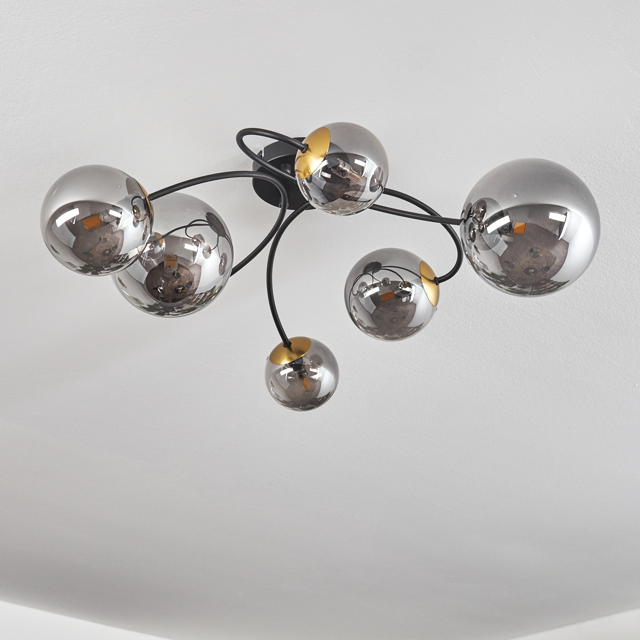 Eine Deckenlampe mit sechs silbernen, reflektierenden Kugeln, schwarzen Armen und goldenen Akzenten auf weißem Hintergrund.