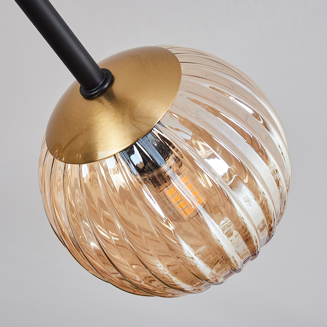 Nahaufnahme einer Leuchte. Sie hat einen goldenen Metallsockel, eine braune Glaskugel mit Spiralmuster und einen schwarzen Arm.