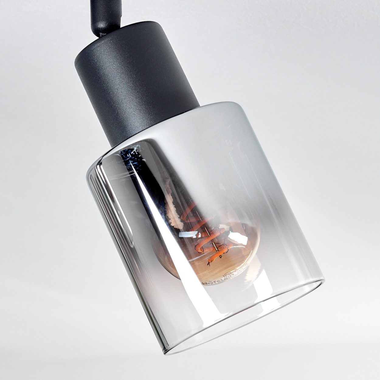 Eine moderne Lampe mit schwarzem Oberteil und einem klaren, zylindrischen Schirm, der eine sichtbare Glühbirne enthält.