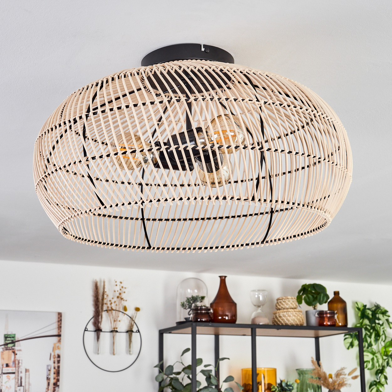 Eine gewebte Deckenlampe aus Rattan hängt. Darunter zeigt ein Regal Dekoration: Vasen, Pflanzen. Die Decke ist weiß, die Lampe beige.