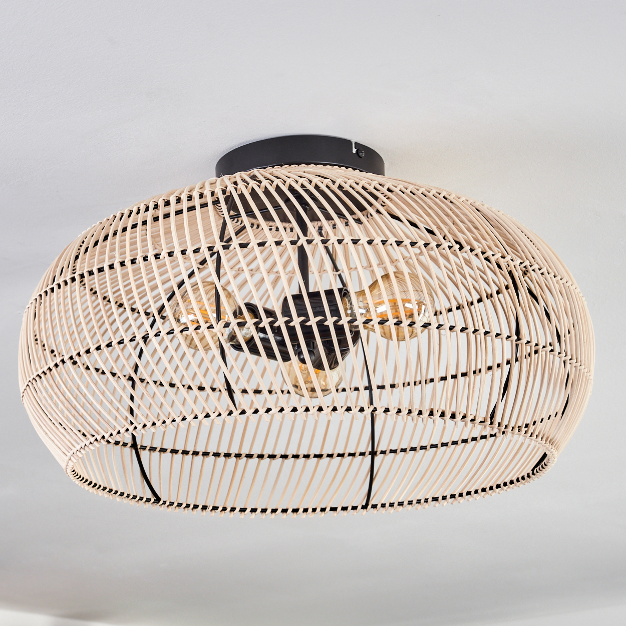 Deckenleuchte aus Korbgeflecht mit drei Glühbirnen und einer schwarzen Halterung an einer weißen Decke.