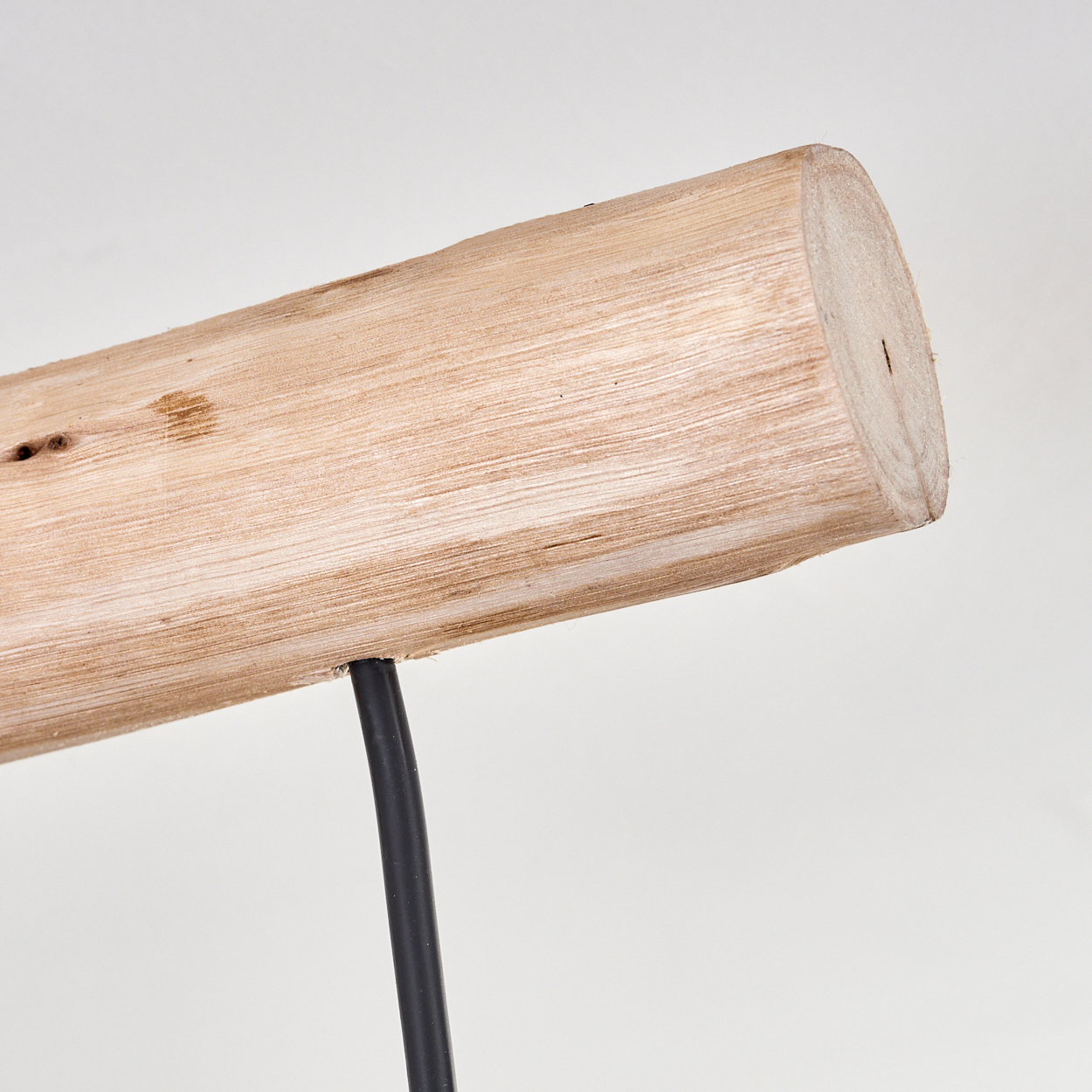 Nahaufnahme eines Holzstamms mit einem schwarzen Draht vor weißem Hintergrund. Der Stamm zeigt Maserung und Äste.