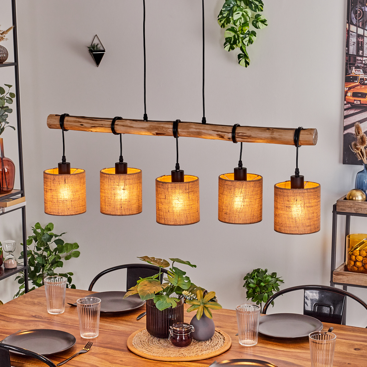 Ein Esszimmer mit Holztisch, Tellern, Gläsern und Pflanzen. Darüber ein Holzbalken mit fünf Lampen.