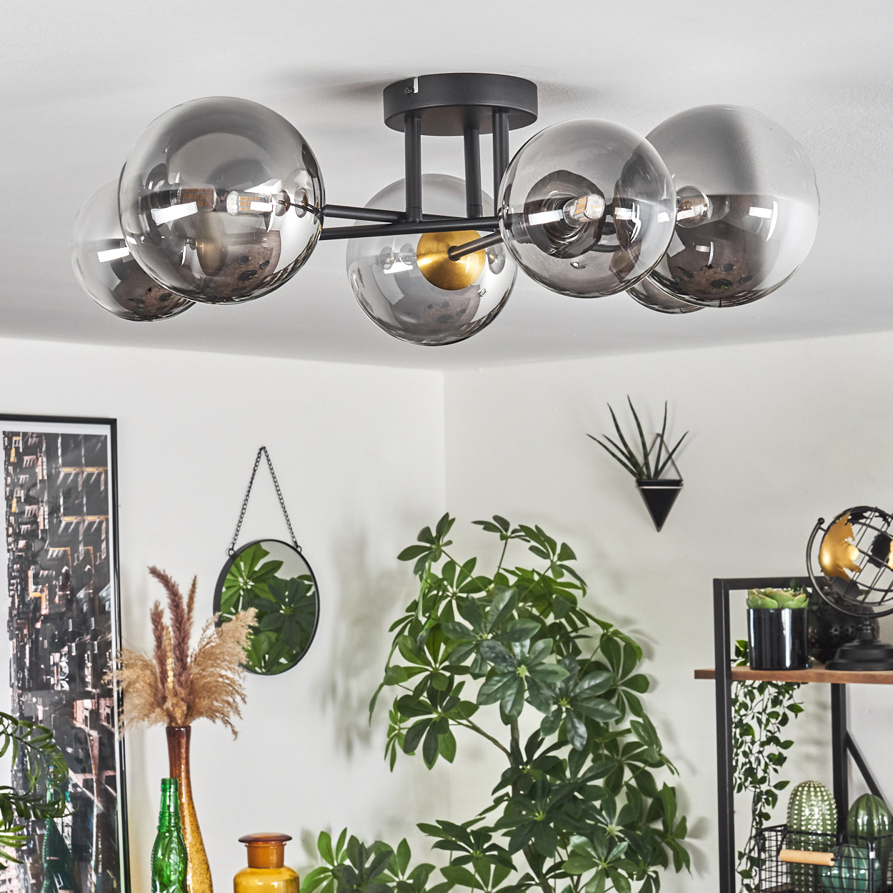 Deckenlampe mit Glaskugeln. Pflanzen, Spiegel und Dekorationsartikel im Raum. Weiße Wand und Decke.