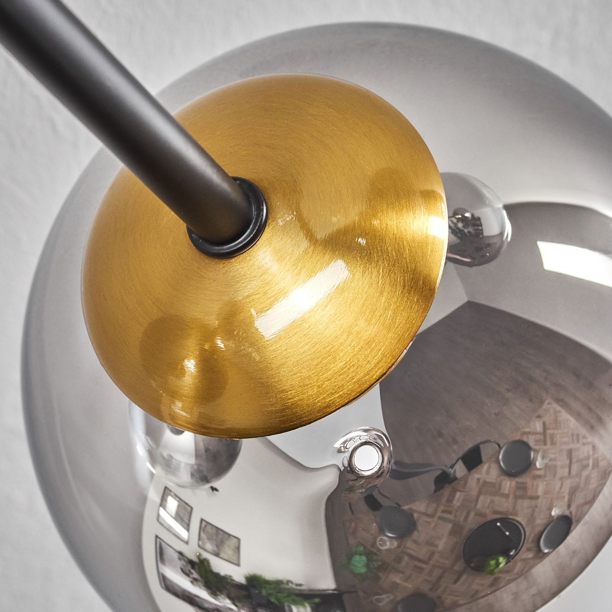 Nahaufnahme einer modernen Lampe mit goldener Scheibe, schwarzem Arm und einer reflektierenden, klaren Glaskugel, die den Raum widerspiegelt.