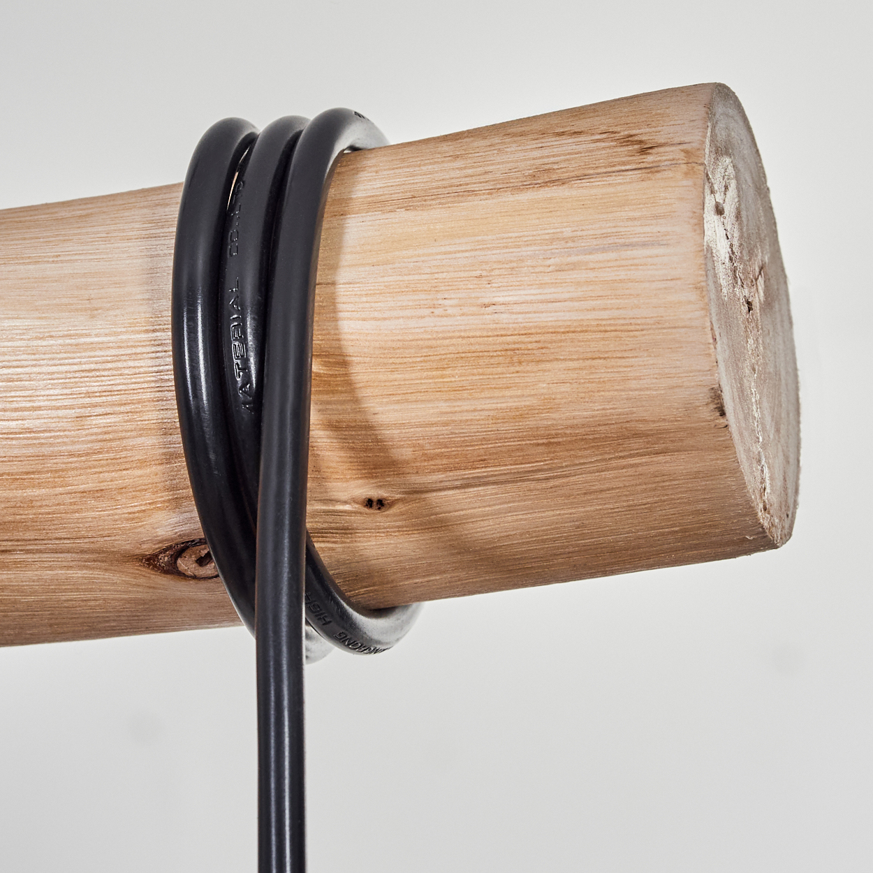Ein Holzstamm mit einem schwarzen Elektrokabel darum gewickelt. Der Hintergrund ist eine schlichte, weiße Wand.