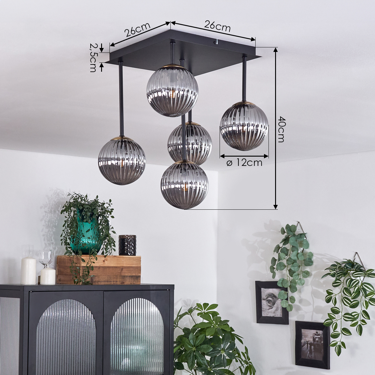 Deckenlampe mit fünf kugelförmigen, gerippten Glasschirmen, die von einem schwarzen quadratischen Sockel hängen. Der Raum hat Pflanzen und einen Schrank.