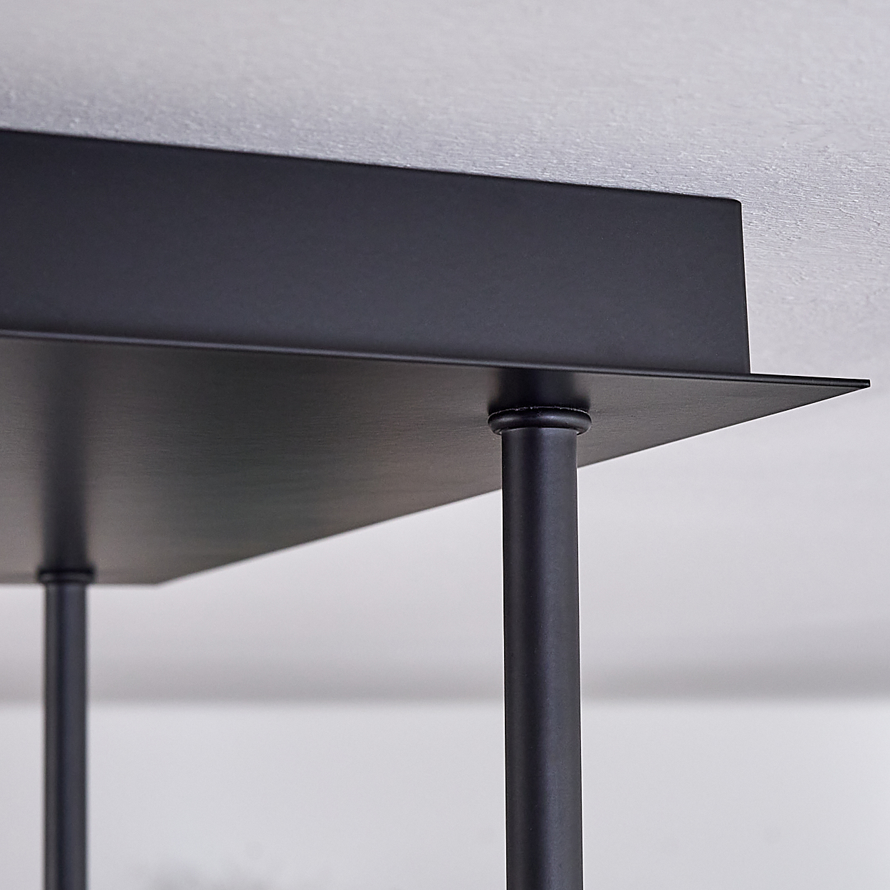 Nahaufnahme einer schwarzen Metallkonstruktion. Eine flache Oberfläche wird von vertikalen zylindrischen Pfosten getragen, alles in Schwarz, vor weißem Hintergrund.