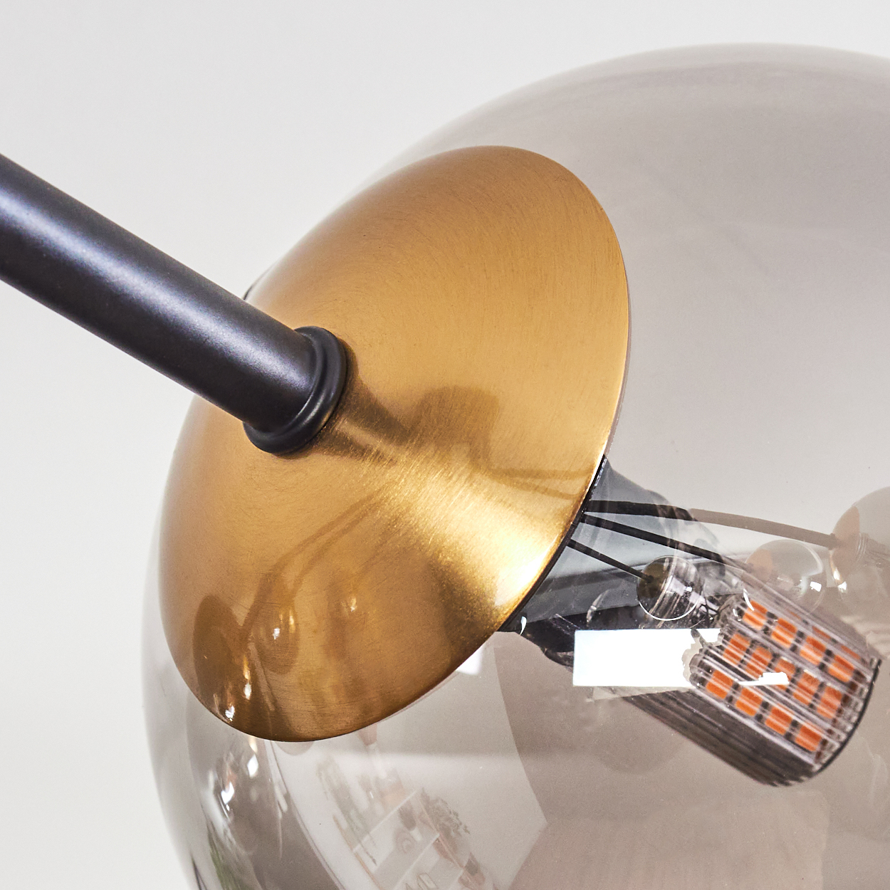 Nahaufnahme einer Lampe mit transparentem Globus, goldfarbenem Sockel und schwarzem Stiel vor weißem Hintergrund. Sichtbare Glühbirne.