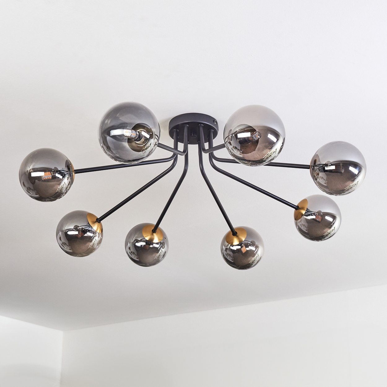 Eine moderne Deckenleuchte mit acht rauchigen Glaskugeln. Schwarze Arme erstrecken sich von einer zentralen Halterung. Das Licht ist an einer weißen Decke montiert.