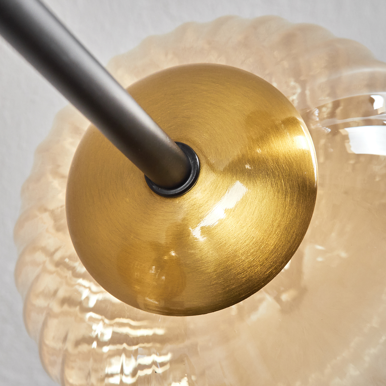 Nahaufnahme einer Messingfarbenen Lampenhalterung mit dunklem Metallarm. Die Lampe hat einen runden Glasschirm.