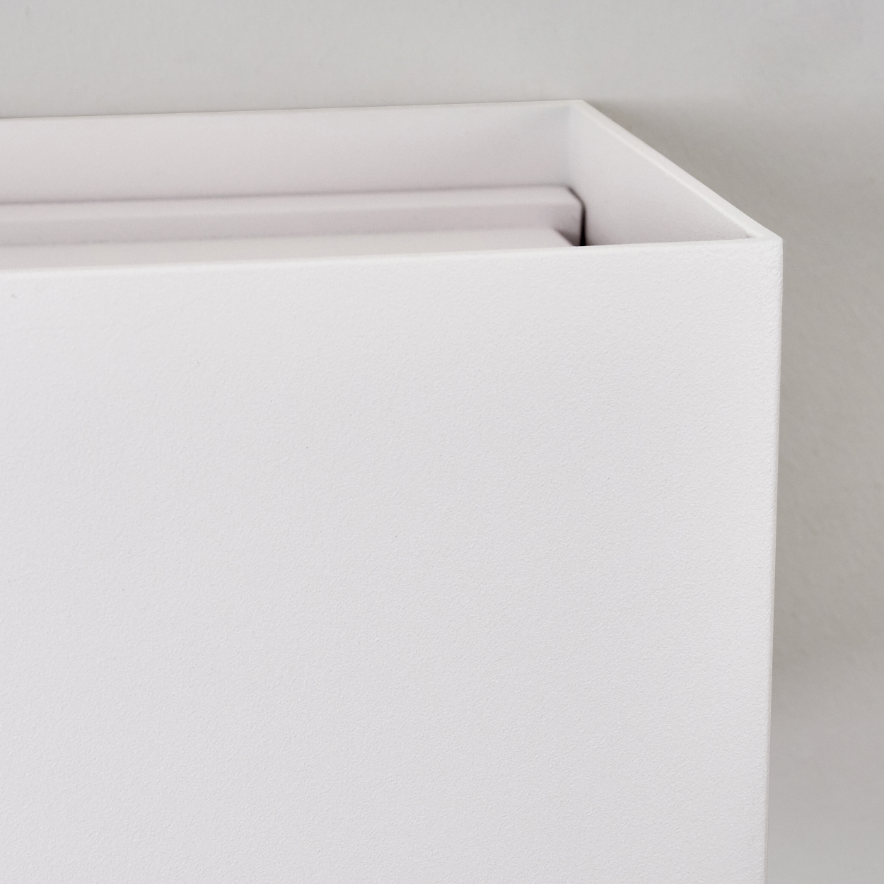 Nahaufnahme einer weißen, rechteckigen Box. Die Box hat eine strukturierte Oberfläche und steht vor einer weißen Wand.