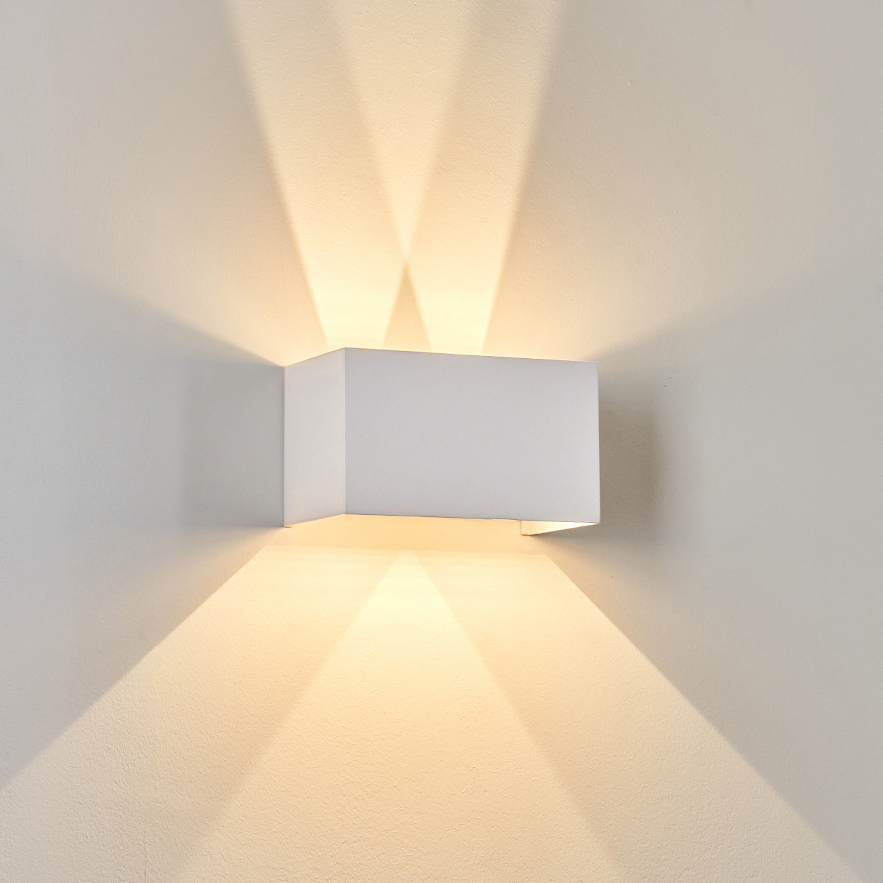 Eine weiße, rechteckige Wandleuchte ist an einer weißen Wand montiert. Lichtstrahlen scheinen nach oben und unten und erzeugen ein symmetrisches Muster.
