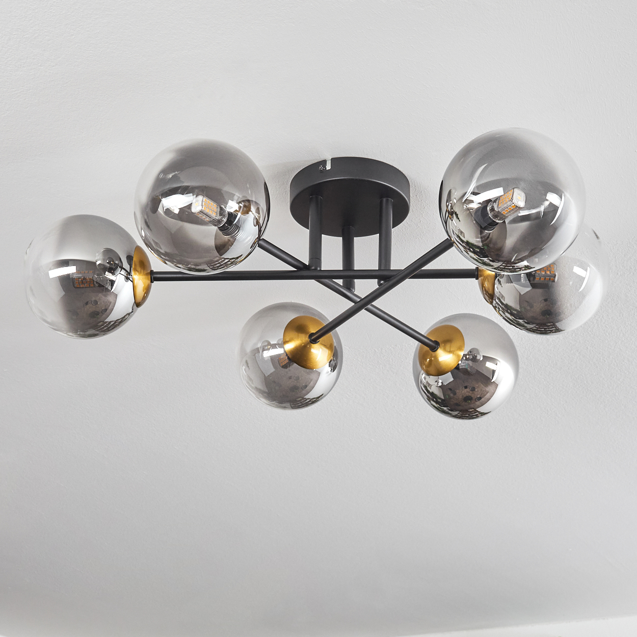 Eine moderne Deckenleuchte mit sechs grauen Glaskugeln, schwarzem Rahmen und goldenen Akzenten, montiert an einer weißen Decke.