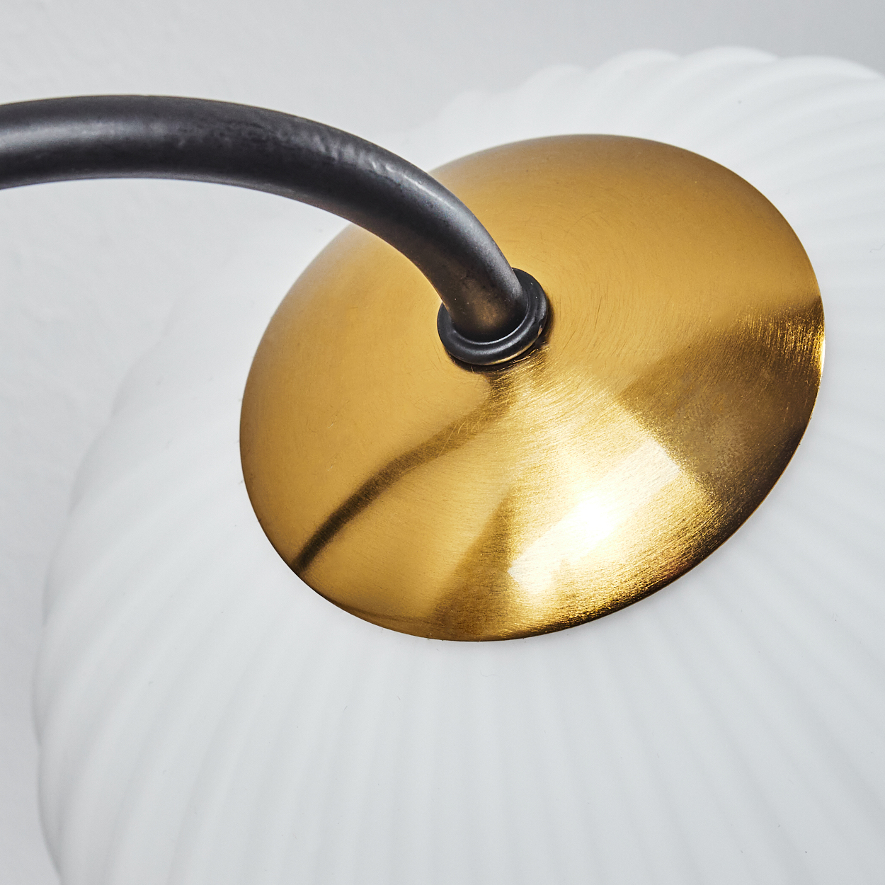 Nahaufnahme einer Lampe. Sie hat einen goldenen Sockel und einen weißen, gerippten Glasschirm. Ein schwarzer Metallarm erstreckt sich vom Sockel.