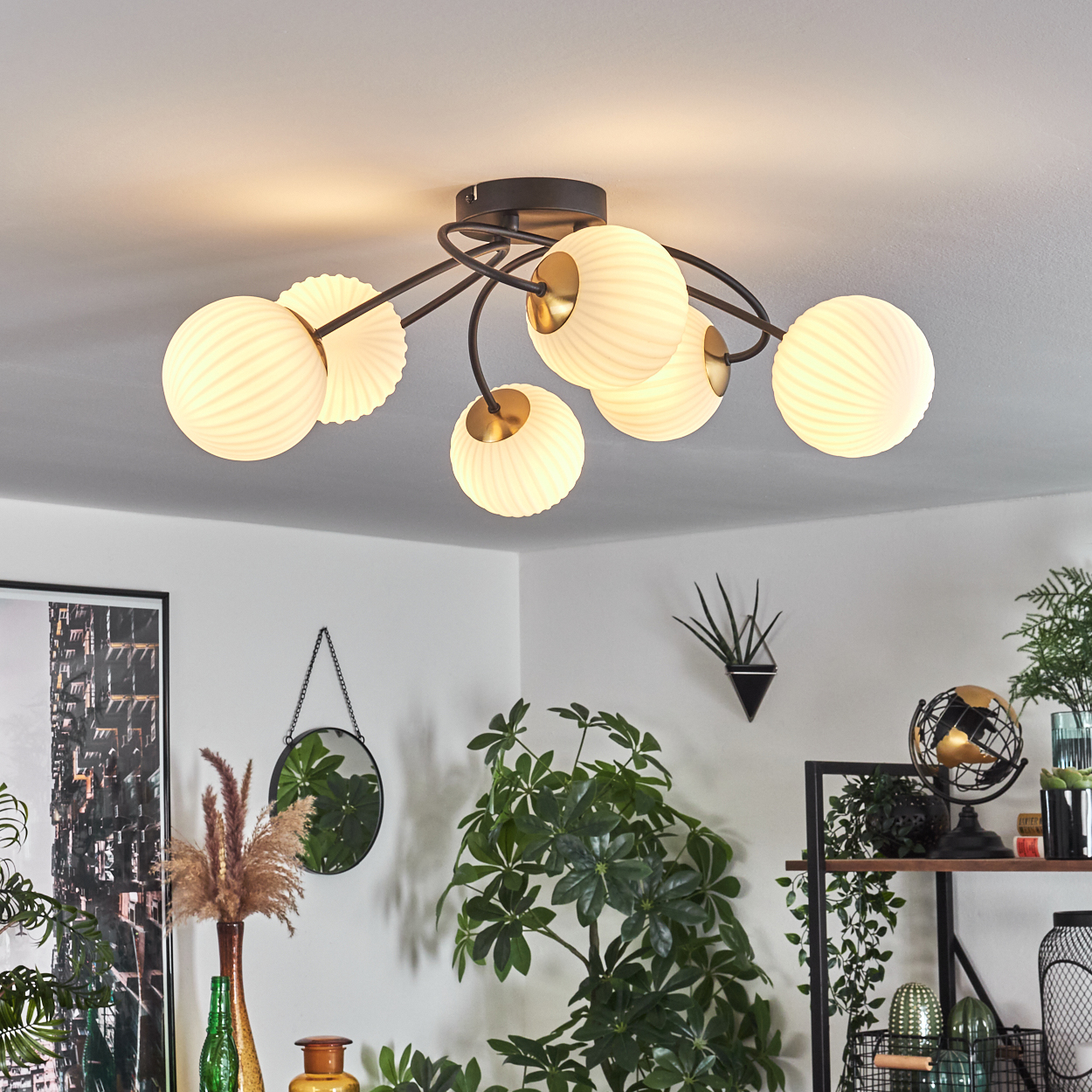 Eine moderne Deckenleuchte mit Glaskugelschirmen. Ein Raum mit Pflanzen und Dekoration ist sichtbar.