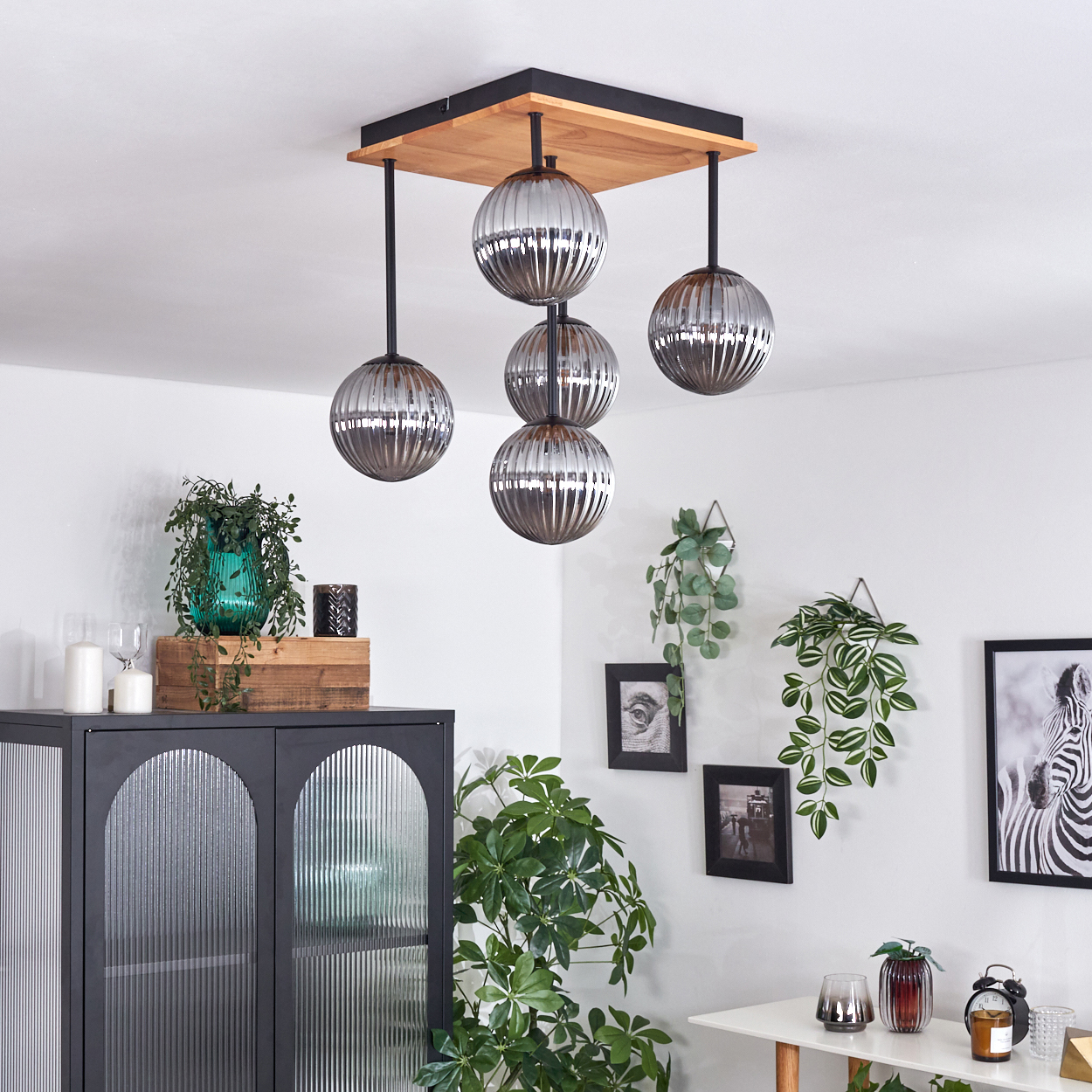 Ein modernes Interieur mit Hängelampen, Pflanzen und Möbeln. Die Lichter sind silberne Kugeln. Ein Zebra-Bild hängt an der Wand.