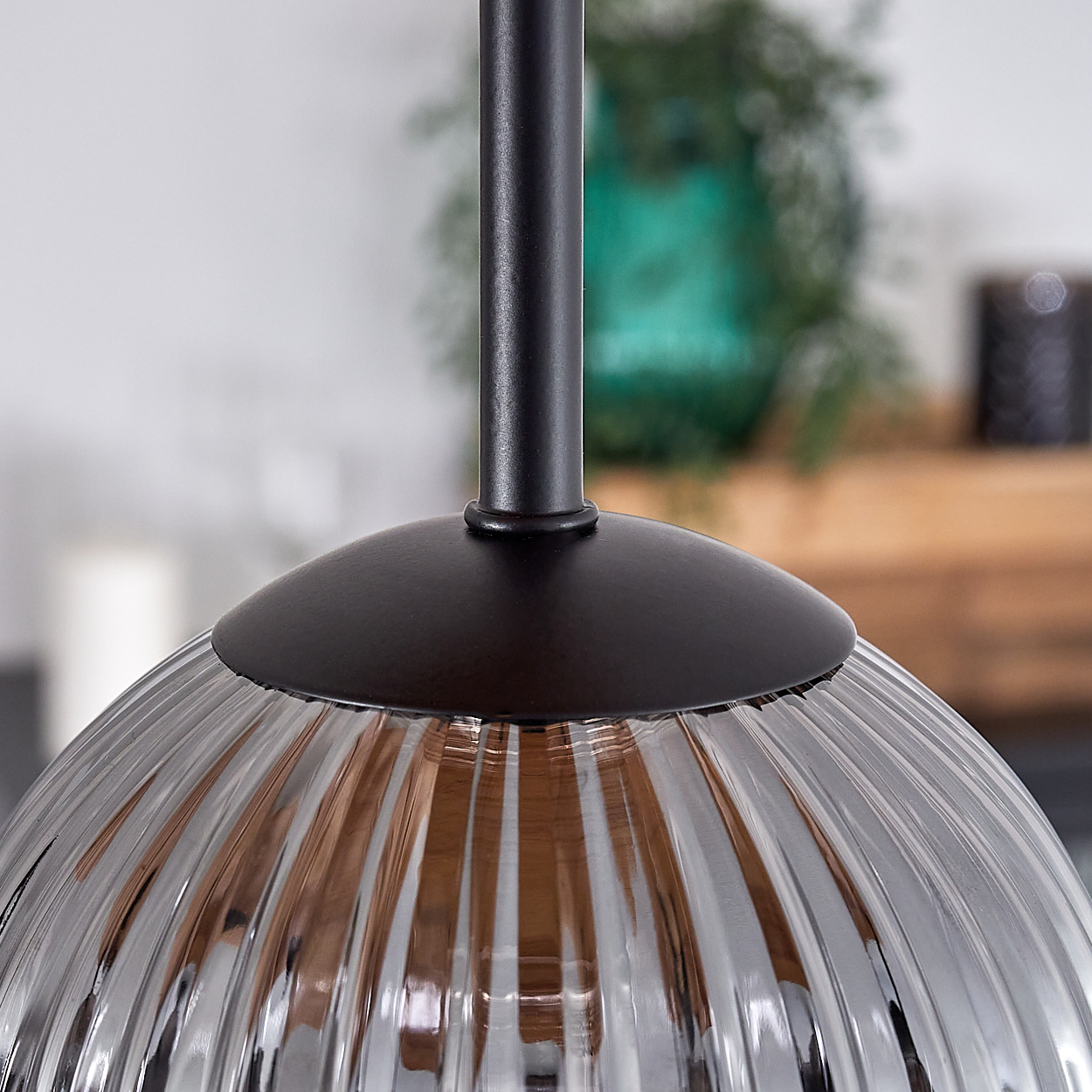 Nahaufnahme eines Lampenschirms aus Glas mit vertikalen Rippen, schwarzem Metallschaft und dunklem Metallsockel. Hintergrund umfasst grüne Vase und Holz.