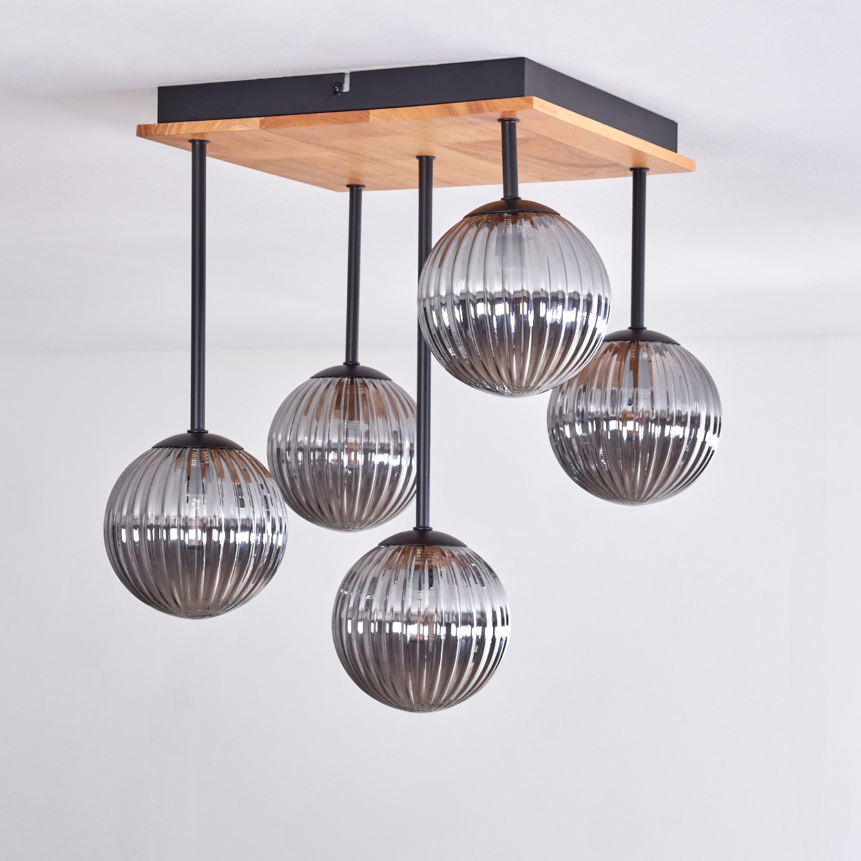 Deckenleuchte mit fünf gerippten Glaskugeln, die von einer Holz- und schwarzen Metallbasis hängen. Weißer Deckenhintergrund.