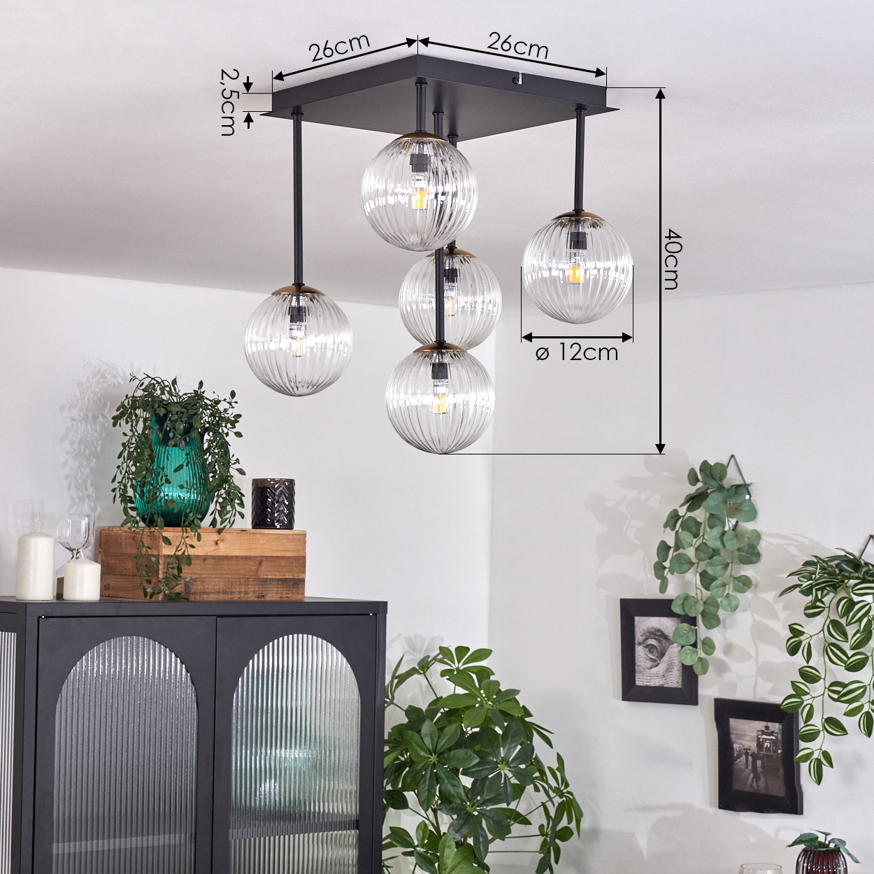 Eine Deckenlampe mit fünf Glaskugelleuchten. Ein schwarzer Schrank mit Pflanzen und gerahmten Bildern sind ebenfalls zu sehen. Weiße Wände ergänzen die Szene.