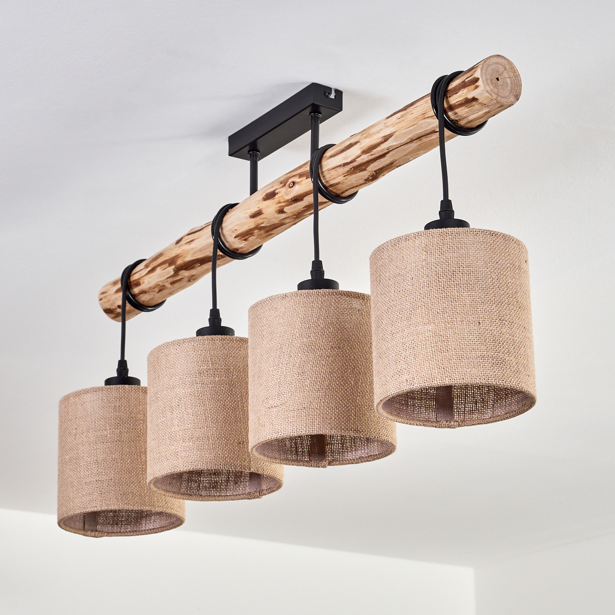 Deckenlampe mit vier beigefarbenen Stoffschirmen, die an einem Holzbalken hängen, schwarze Drähte und eine weiße Decke.