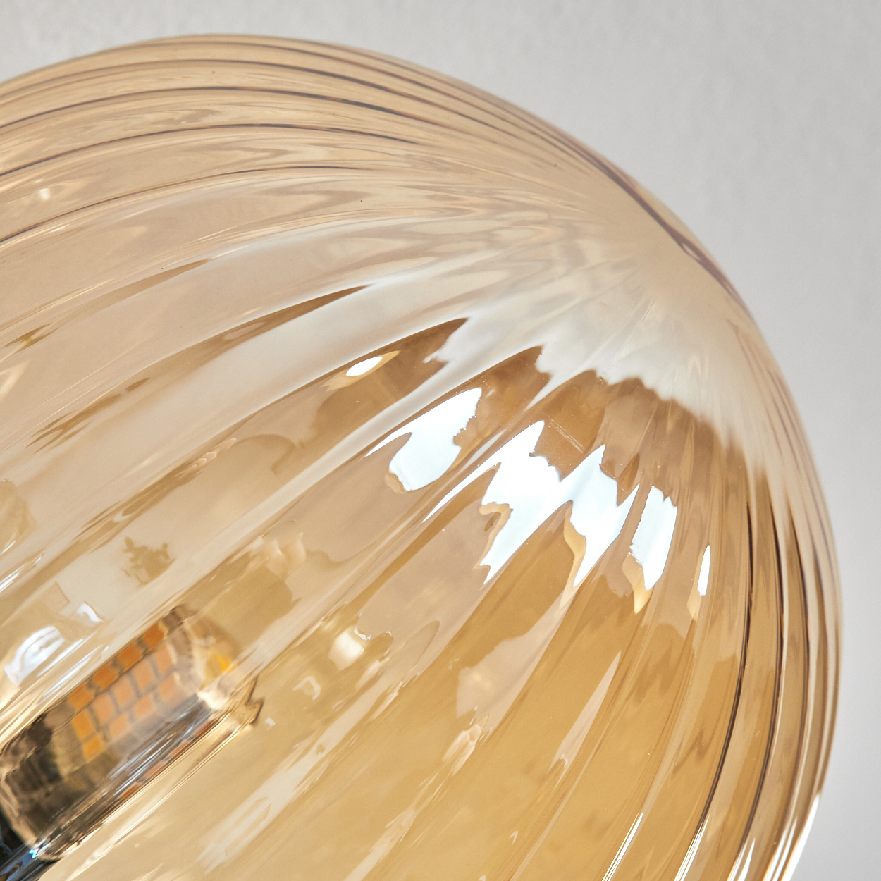 Nahaufnahme einer Glasleuchte. Das bernsteinfarbene Glas hat ein geripptes Muster. Der Hintergrund ist eine schlichte weiße Wand.