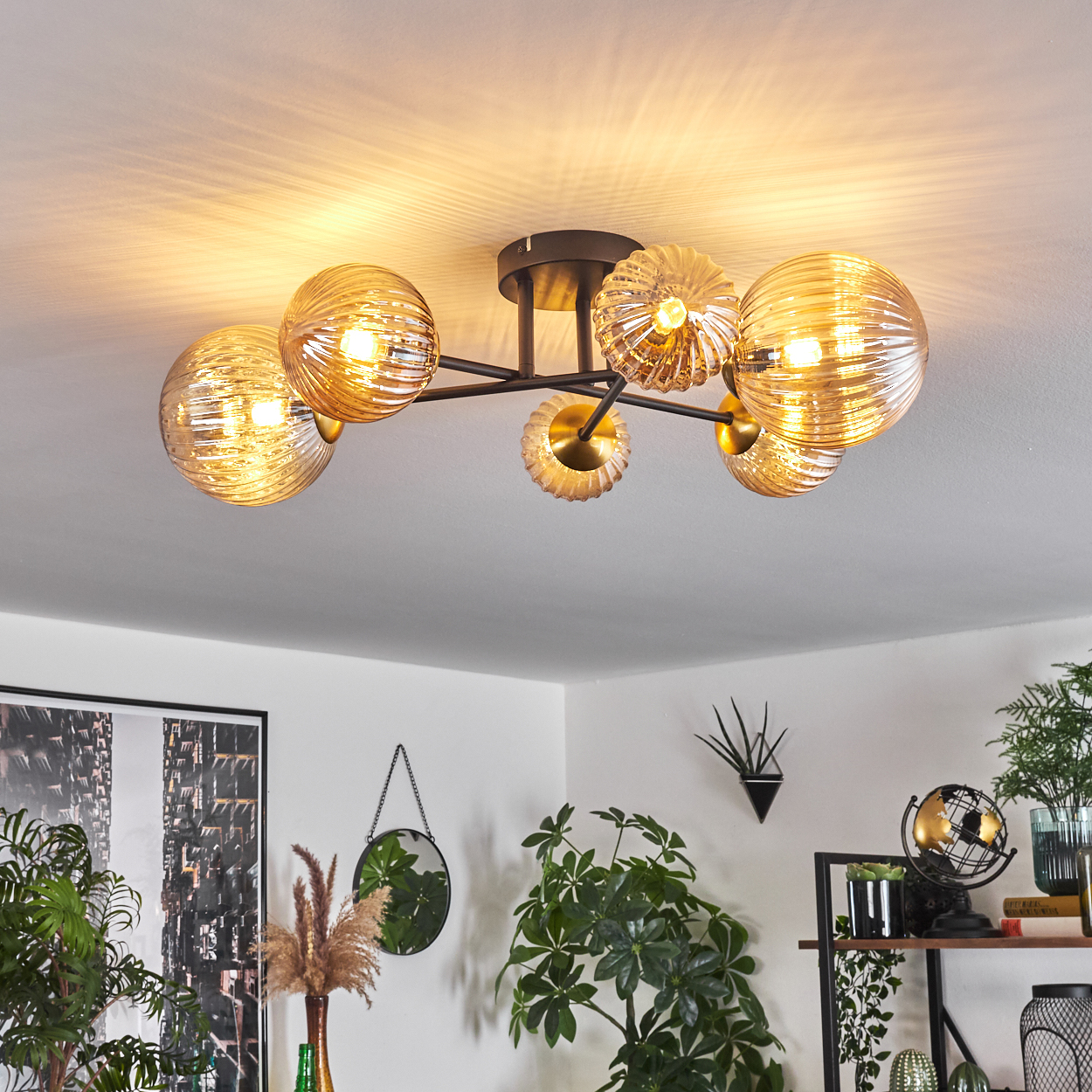 Deckenleuchte mit Glaskugeln, schwarzer Rahmen. Pflanzen, Spiegel und Kunstwerk im Hintergrund. Warmes Licht, weiße Decke.