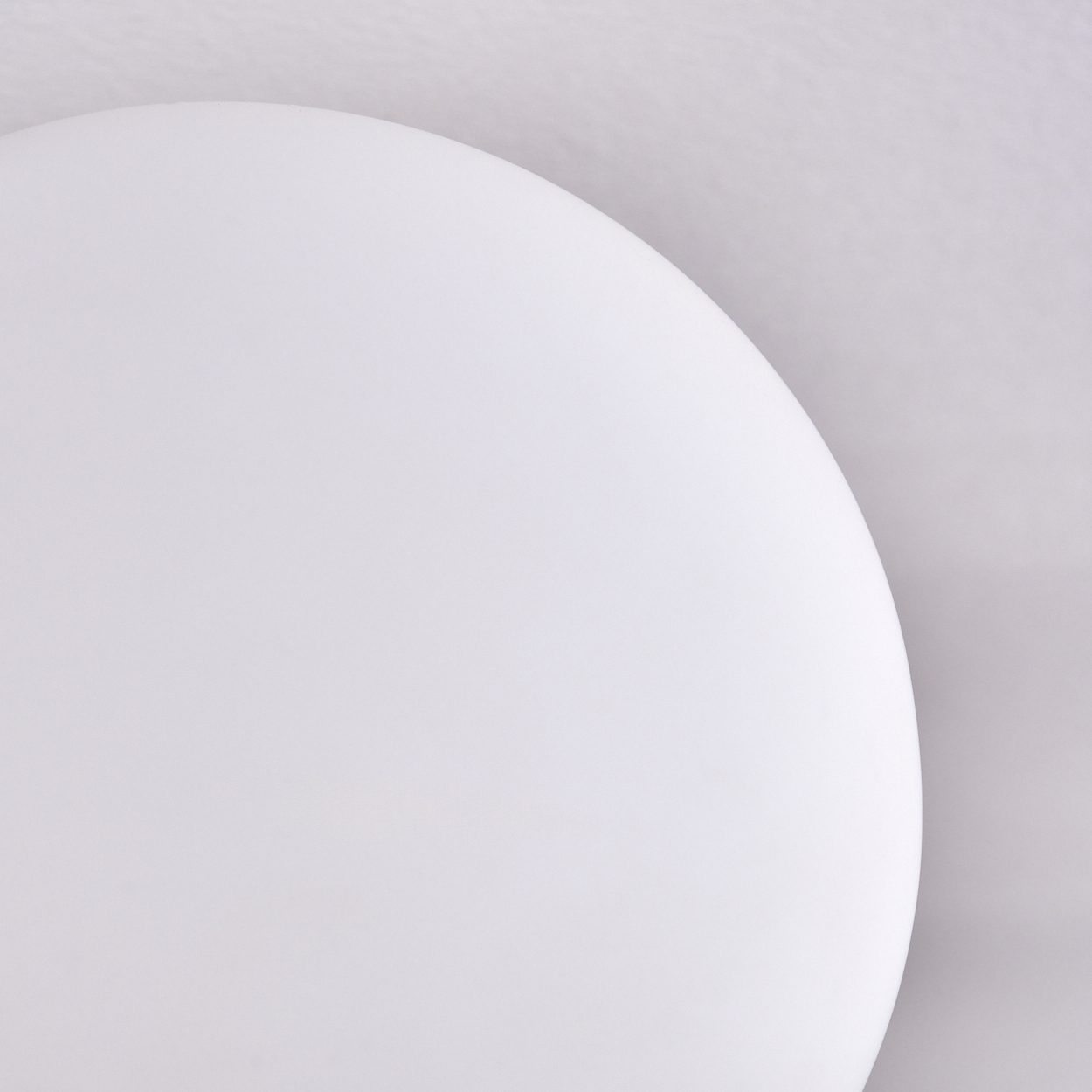 Nahaufnahme zeigt ein weißes, kreisförmiges Objekt, möglicherweise eine Lampe oder ein Teller, vor hellgrauem Hintergrund.