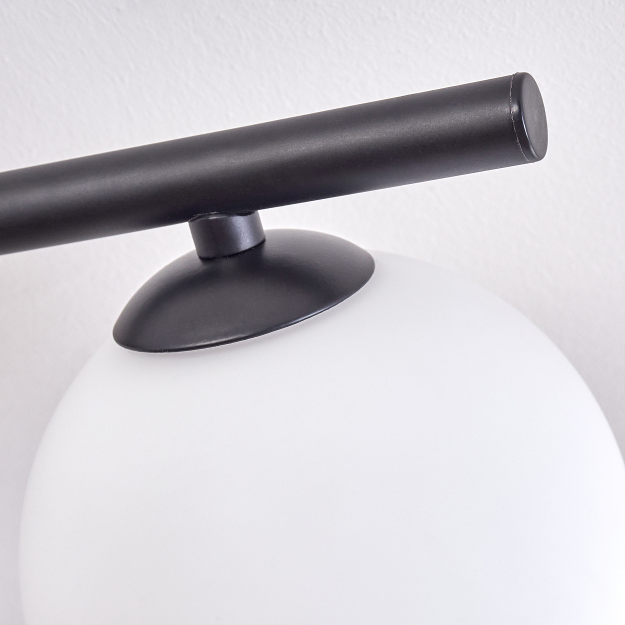 Eine moderne Lampe mit schwarzem Metallarm und weißem, kugelförmigem Glasschirm. Der Hintergrund ist eine schlichte, weiße Wand.