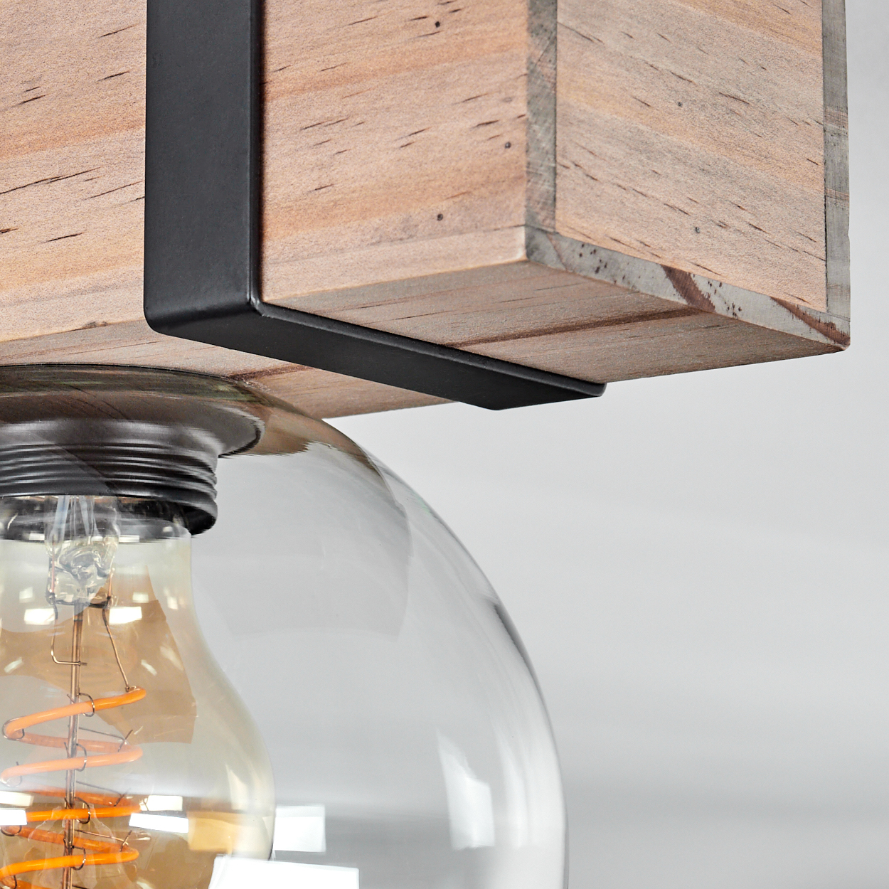 Nahaufnahme einer Leuchte. Ein Holzbalken wird von schwarzen Metallstützen gehalten. Ein Glaskolben umschließt eine Edison-Glühbirne.