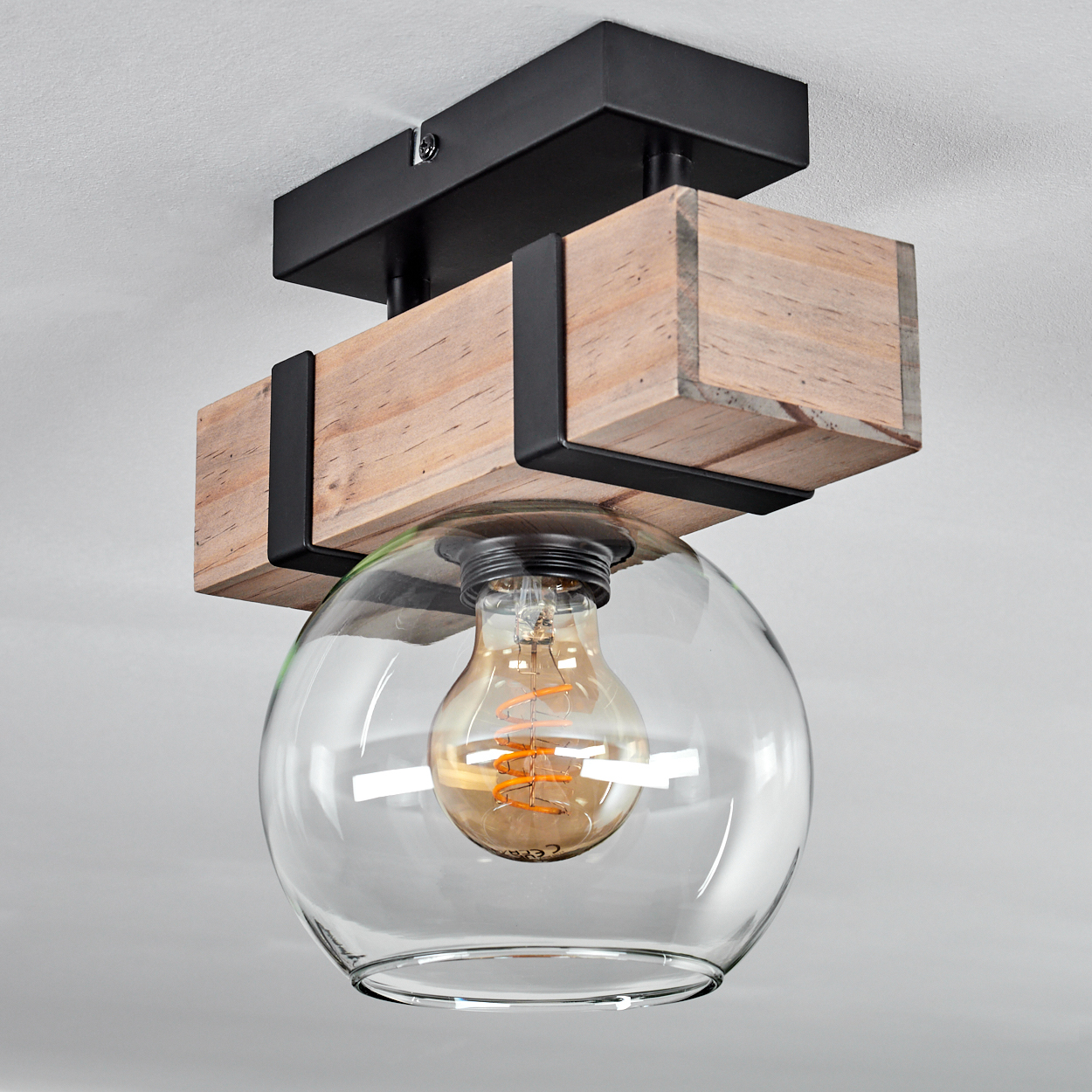 Eine Deckenleuchte mit Holzbalken, schwarzen Metallstützen und einer Glaskugel, die eine Glühbirne umschließt.