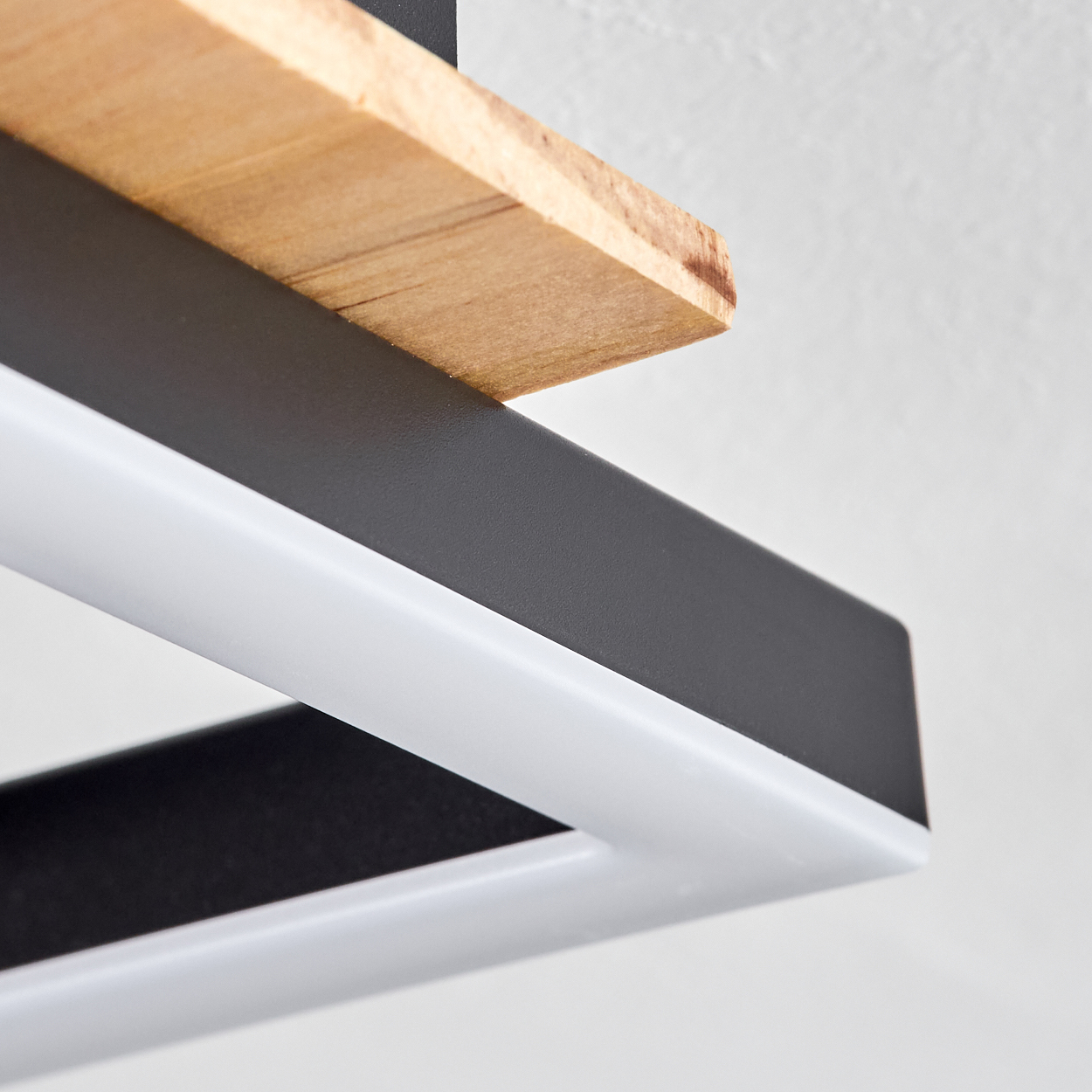 Nahaufnahme einer modernen Leuchte. Sie hat eine Holzplatte, einen schwarzen Rahmen und einen weißen Lichtbereich. Der Hintergrund ist eine schlichte weiße Wand.