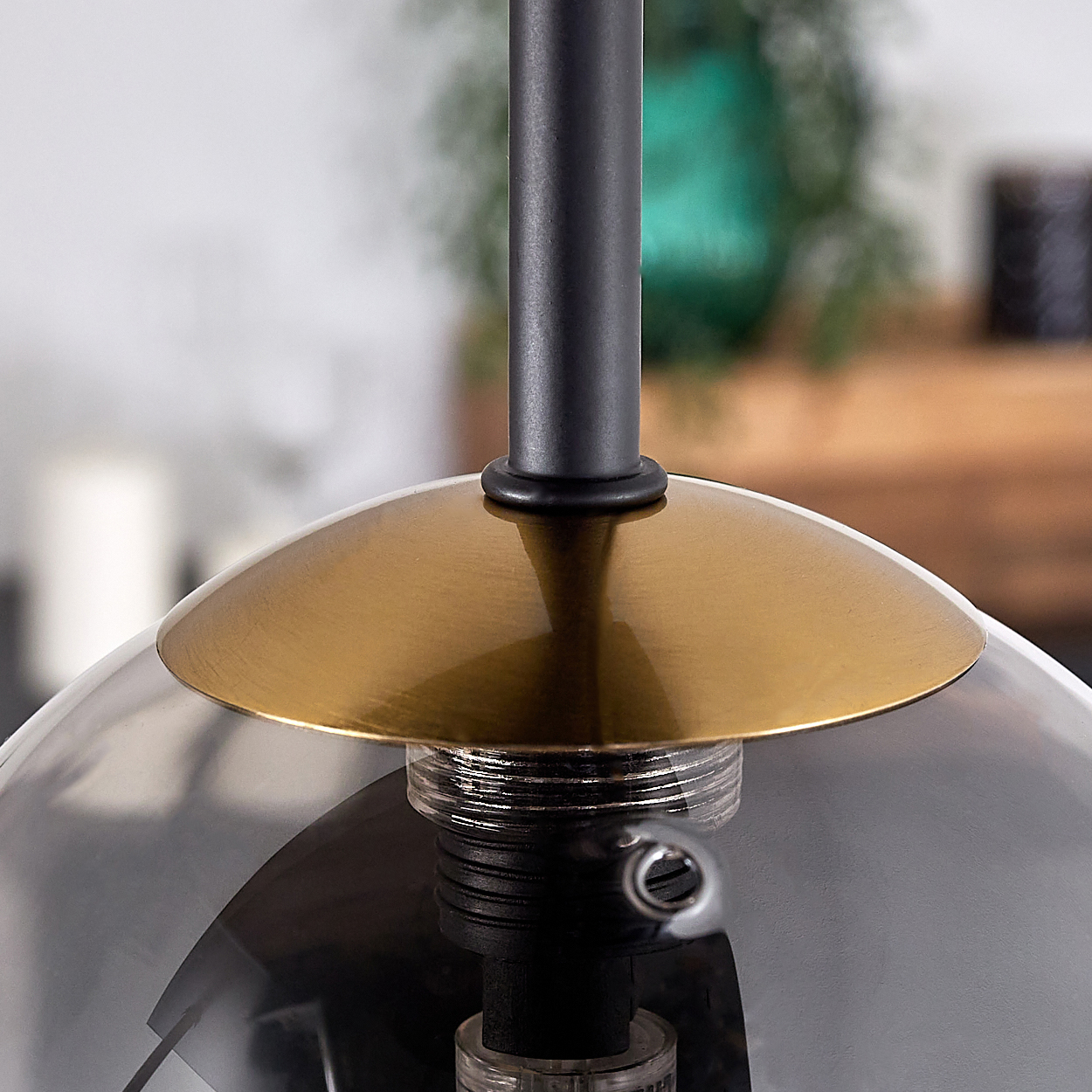 Nahaufnahme einer modernen Lampe. Sie hat einen goldfarbenen Schirm und eine klare Glaskugel mit dunklem Metallschaft.