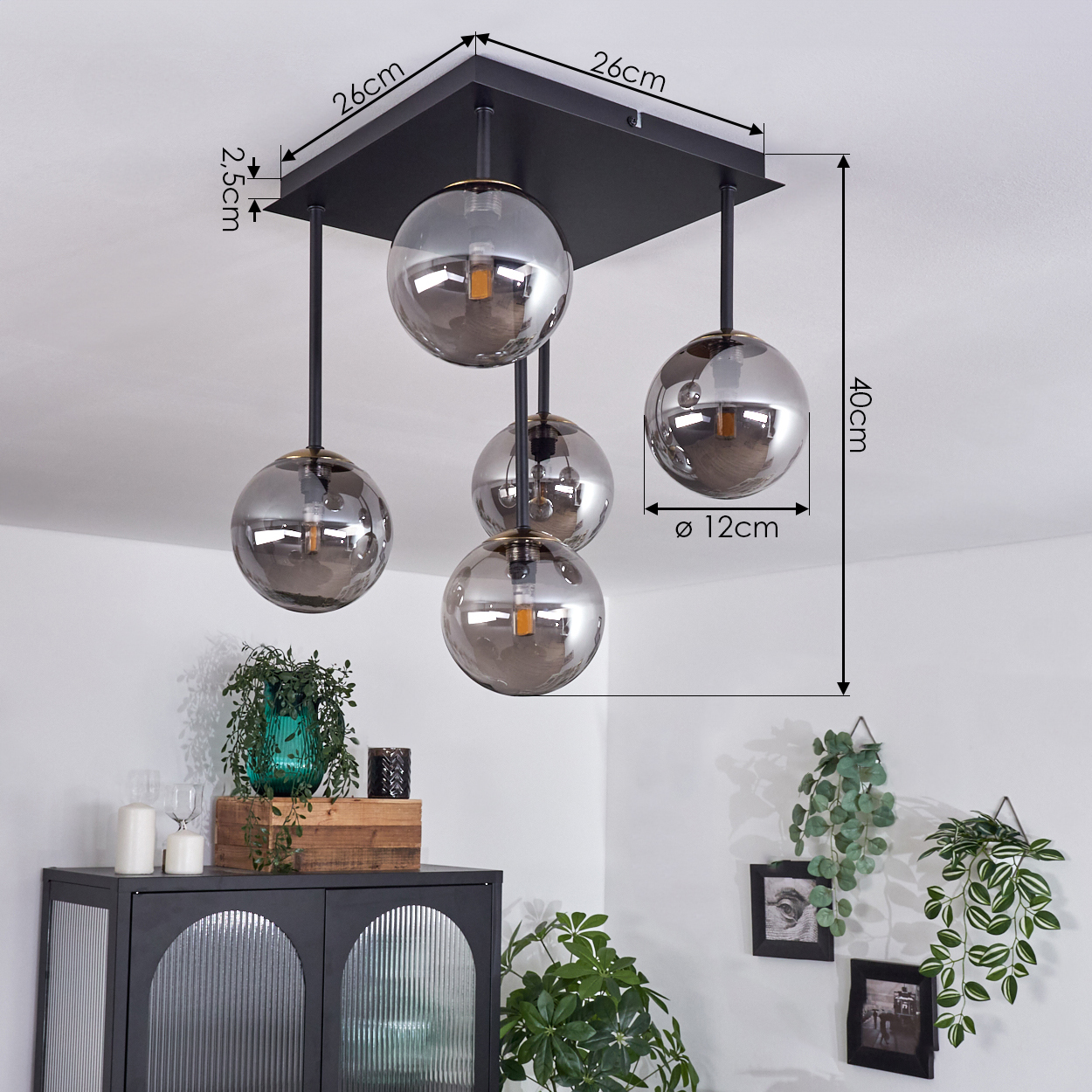 Eine schwarze Deckenlampe mit fünf grauen Glaskugelschirmen. Maße werden angezeigt. Hintergrund zeigt weiße Wände, Dekoration und Möbel.