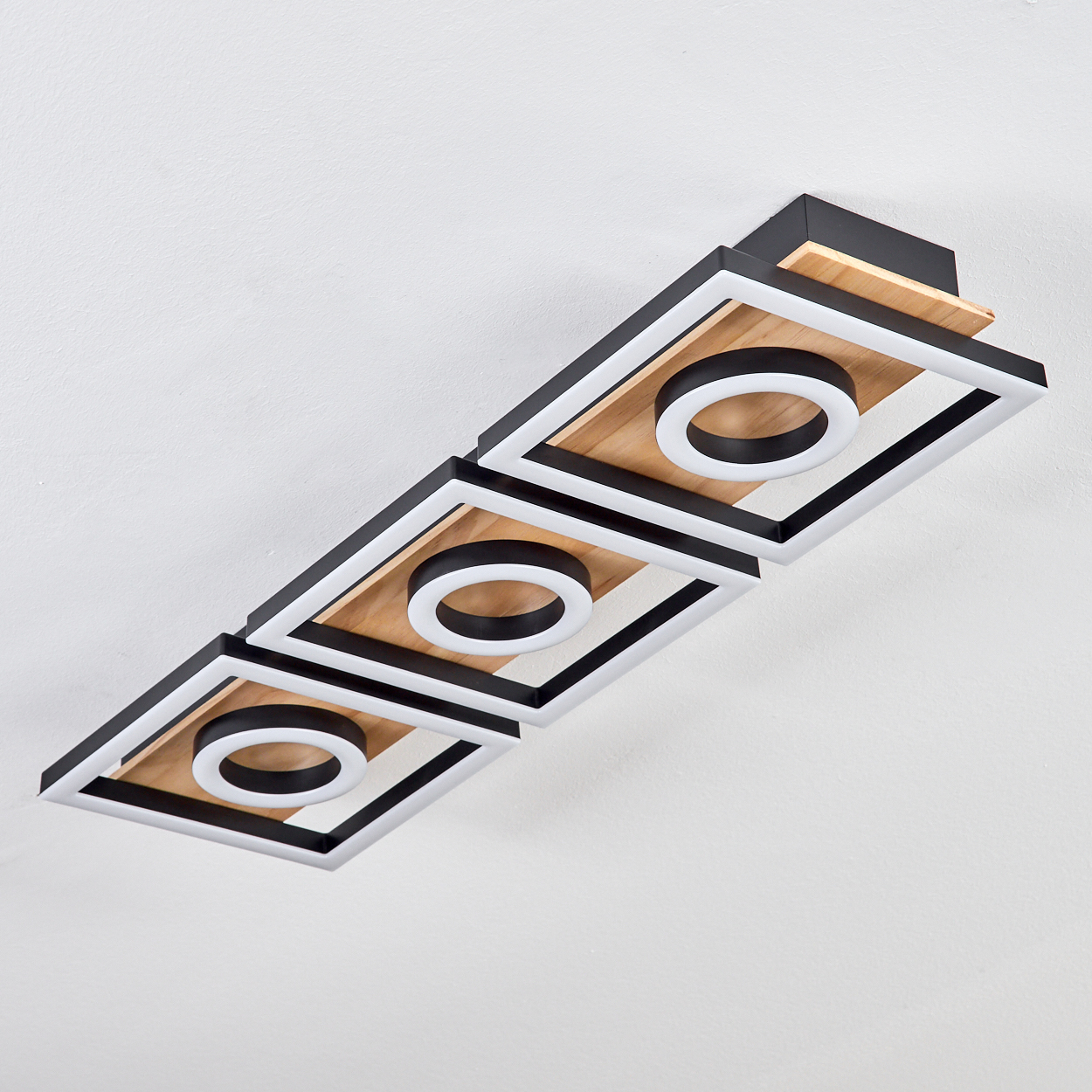 Eine moderne Deckenleuchte mit drei quadratischen Rahmen. Jeder Rahmen hat eine Holzplatte, einen schwarzen Rahmen und ein weißes Ringlicht.