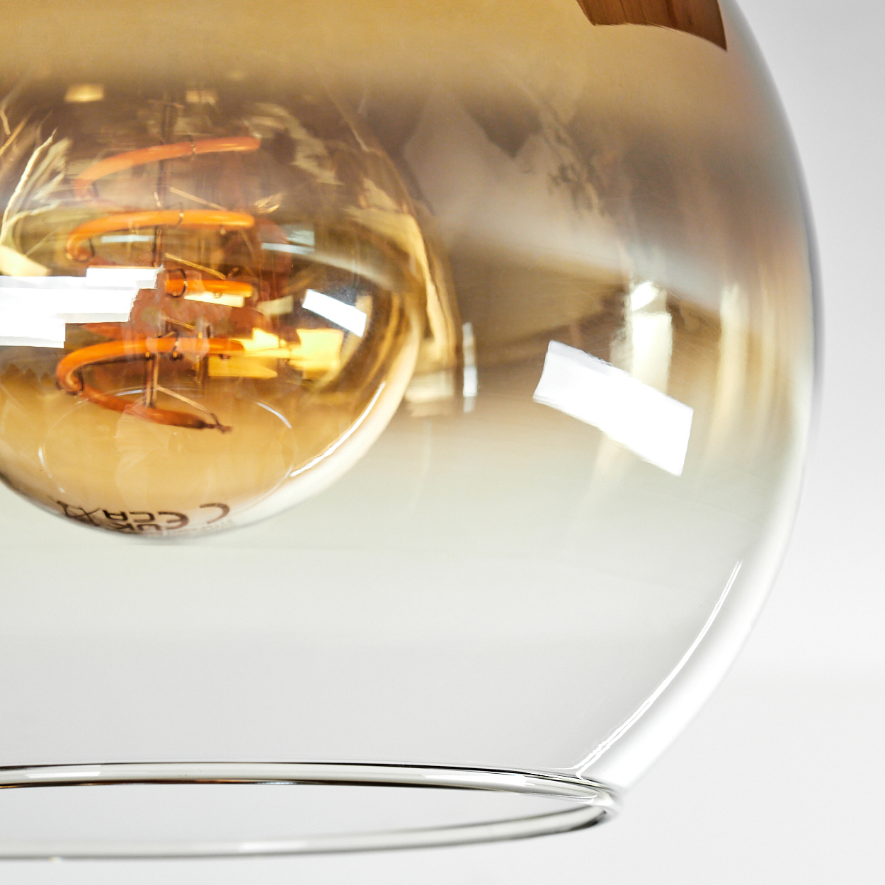Nahaufnahme einer Leuchte. Eine transparente Glaskugel mit einer warm getönten Glühbirne. Das Glas hat einen Farbverlauf.