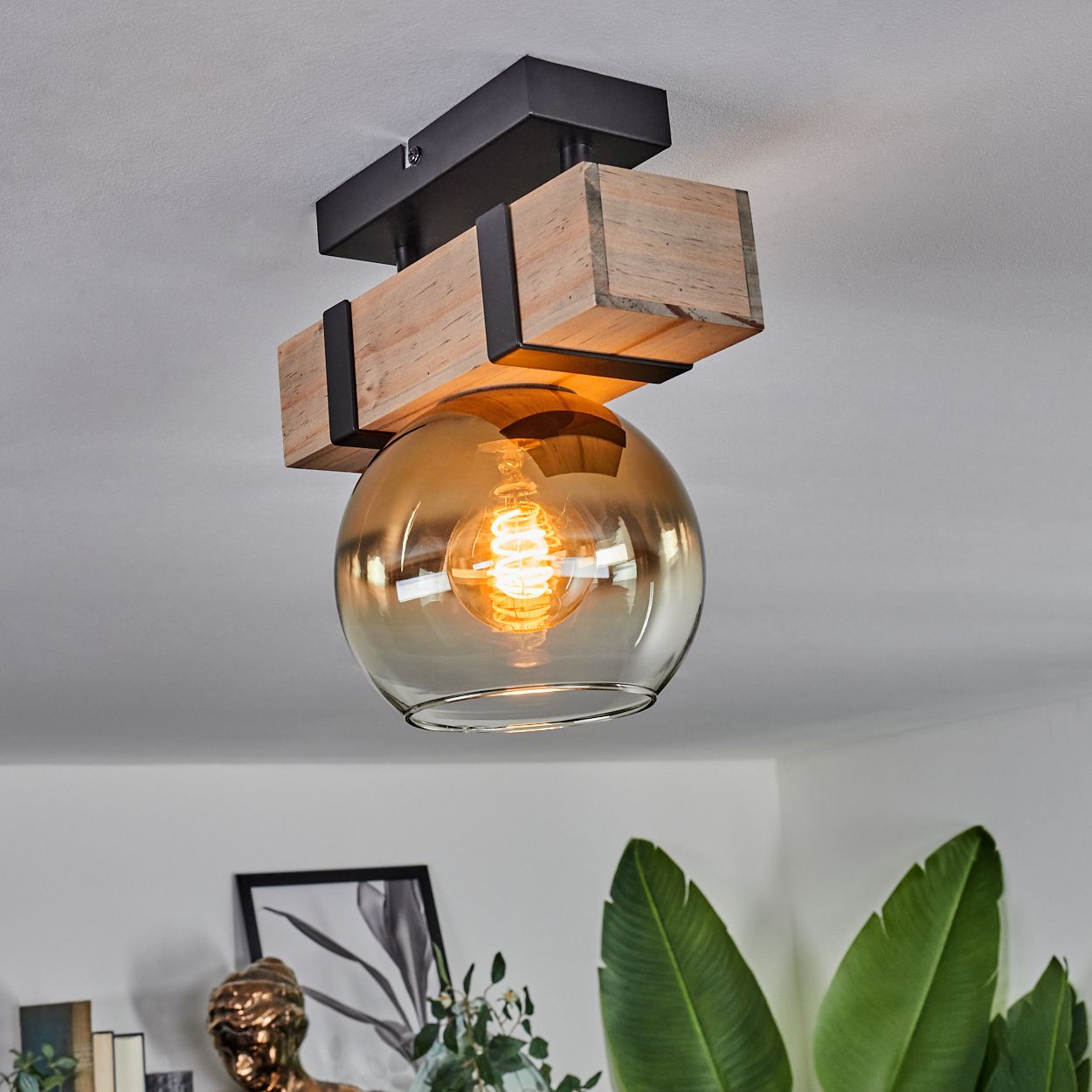 Eine Deckenleuchte mit Holzbalken-Design und einer kugelförmigen, bernsteinfarbenen Glaskugel. Im Inneren befindet sich eine leuchtende Glühbirne.