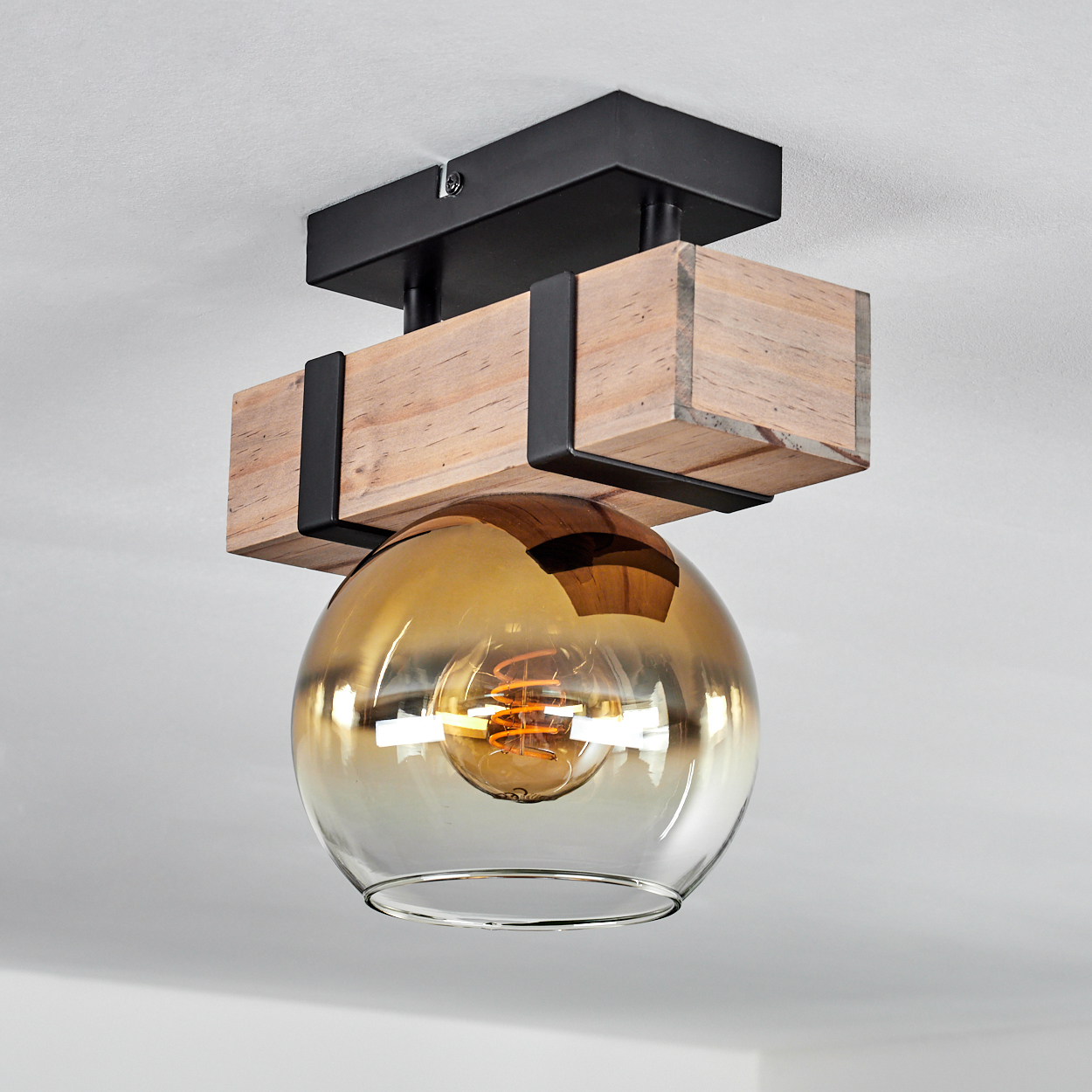 Deckenleuchte mit Holzbalken, schwarzen Metallhaltern und einem kugelförmigen bernsteinfarbenen Glasschirm mit Glühbirne.