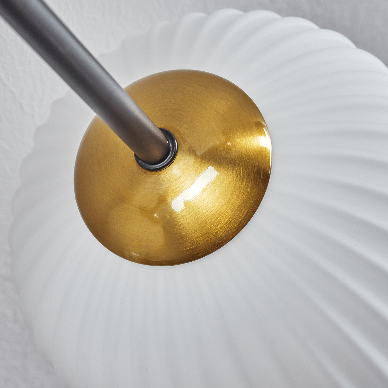 Nahaufnahme einer modernen Lampe. Eine messingfarbene Scheibe ist mit einem weißen, geriffelten Glasschirm verbunden, mit einem dunklen Metallarm.
