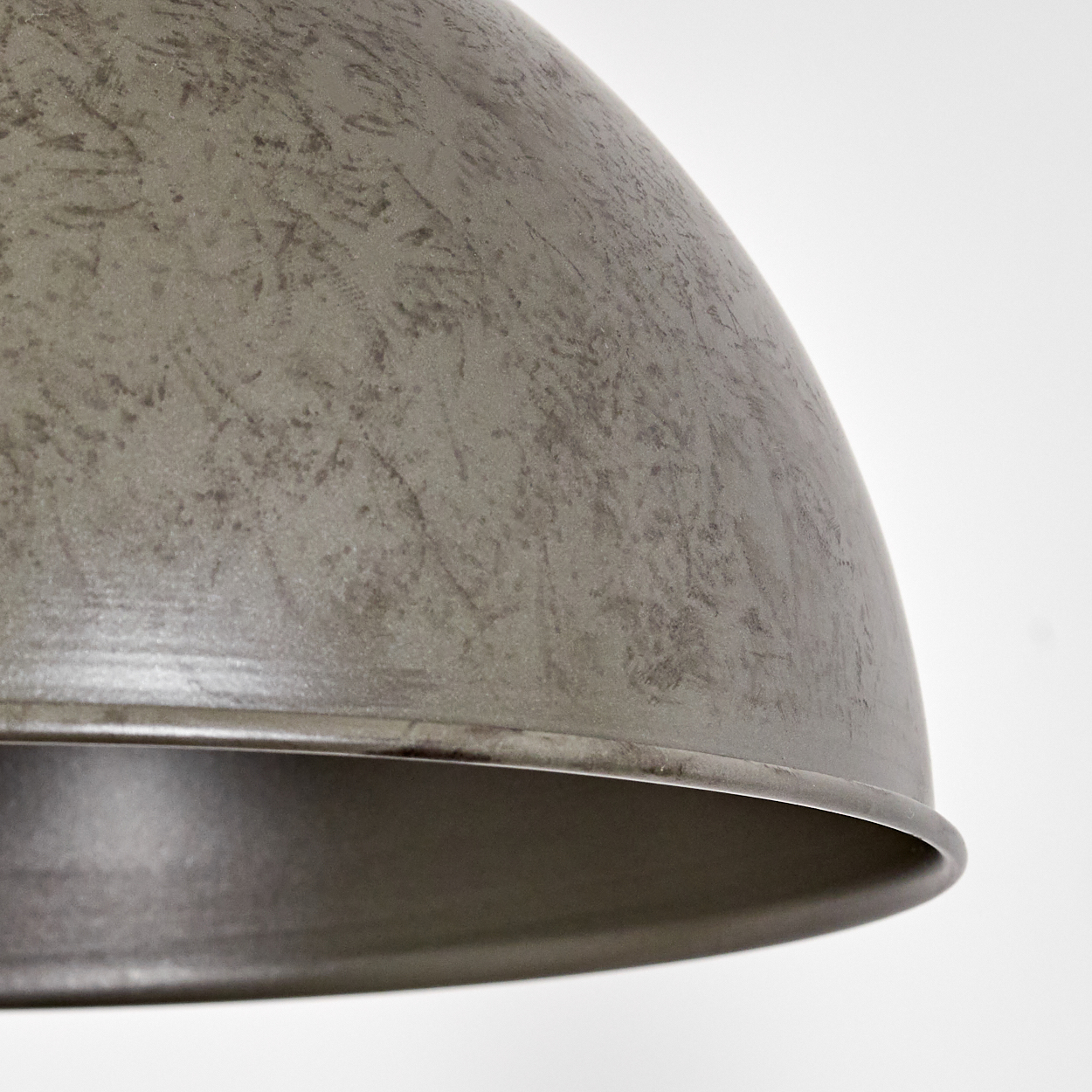 Nahaufnahme eines verwitterten, grauen Metalllampenschirms vor weißem Hintergrund. Der Schirm hat ein gebogenes Design mit strukturierter Oberfläche.