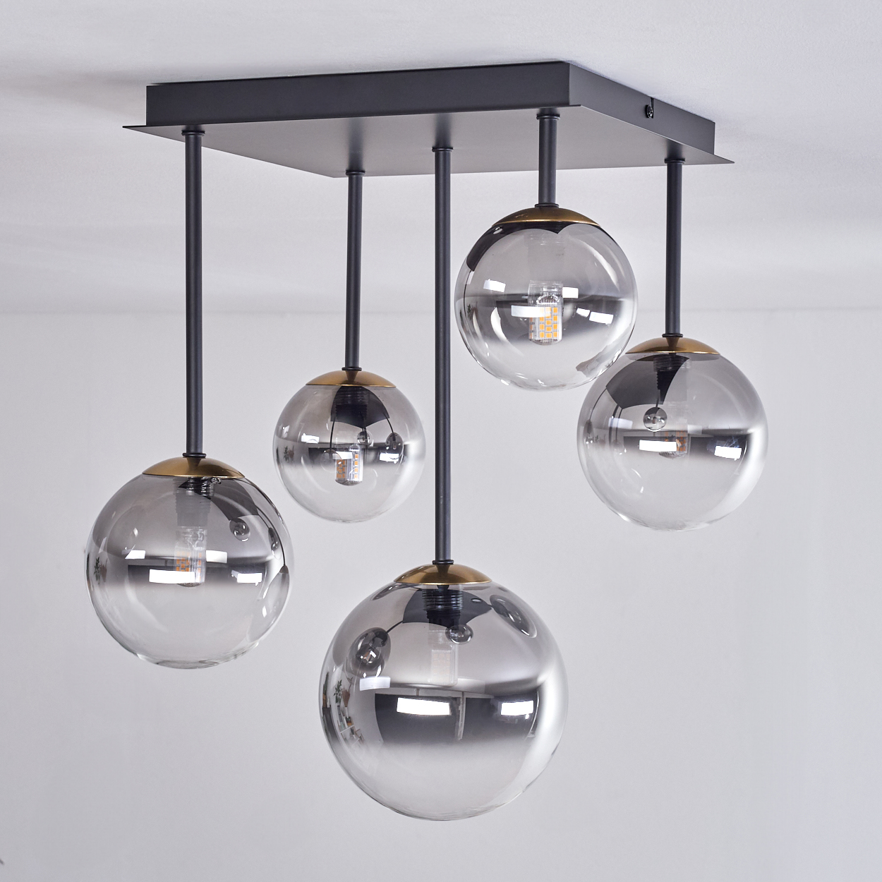 Moderne Deckenleuchte mit fünf kugelförmigen Glasschirmen. Die Leuchte hat schwarze Stangen und eine quadratische Basis sowie Messingakzente.