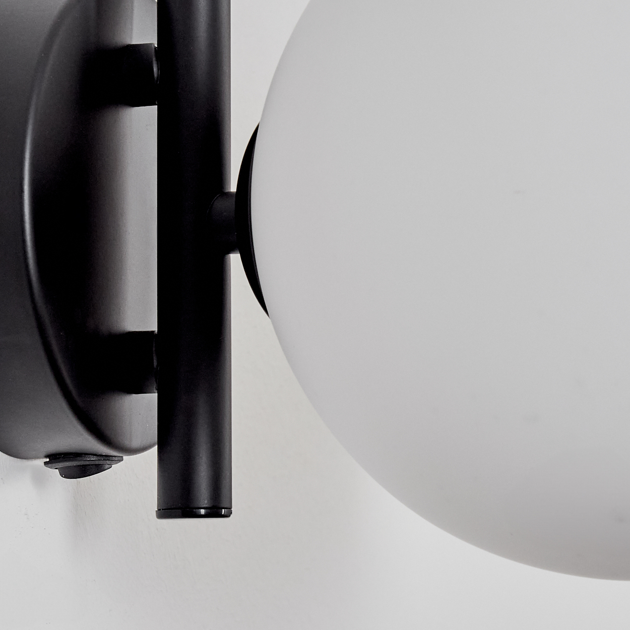 Eine schwarze Wandleuchte mit einem weißen Globus. Die Leuchte hat einen runden Sockel und einen zylindrischen Arm. Der Hintergrund ist weiß.