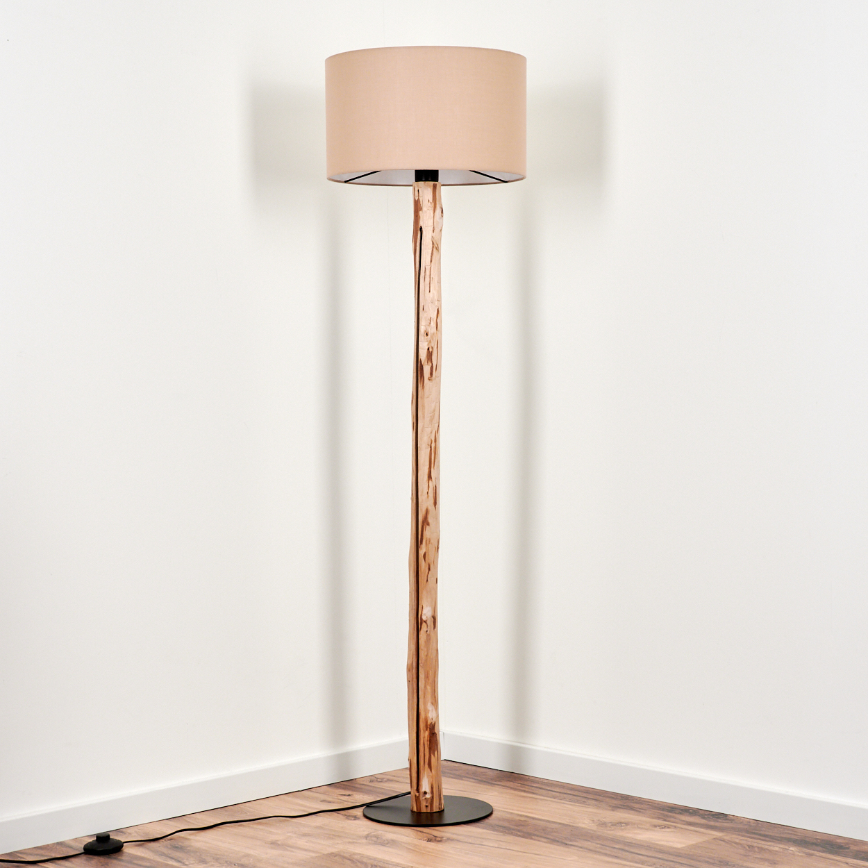 Eine Stehlampe steht in einer Ecke. Sie hat einen beigen Lampenschirm und einen holzartigen Stamm. Der Hintergrund ist weiß.