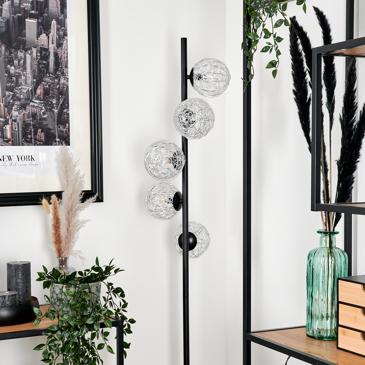 Ein modernes Wohnzimmer. Es zeigt eine schwarze Lampe mit kugelförmigen Lichtern, ein gerahmtes New York-Bild und dekorative Pflanzen.