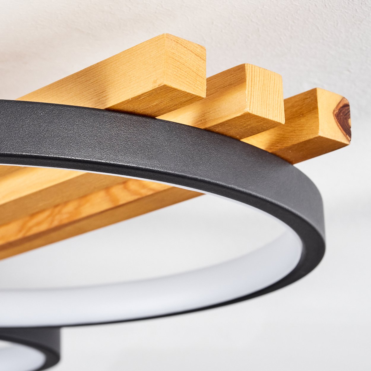 Eine moderne Deckenlampe mit Holzbalken und einem schwarzen Ring. Die Lampe hat ein weißes Licht und eine weiße Decke.