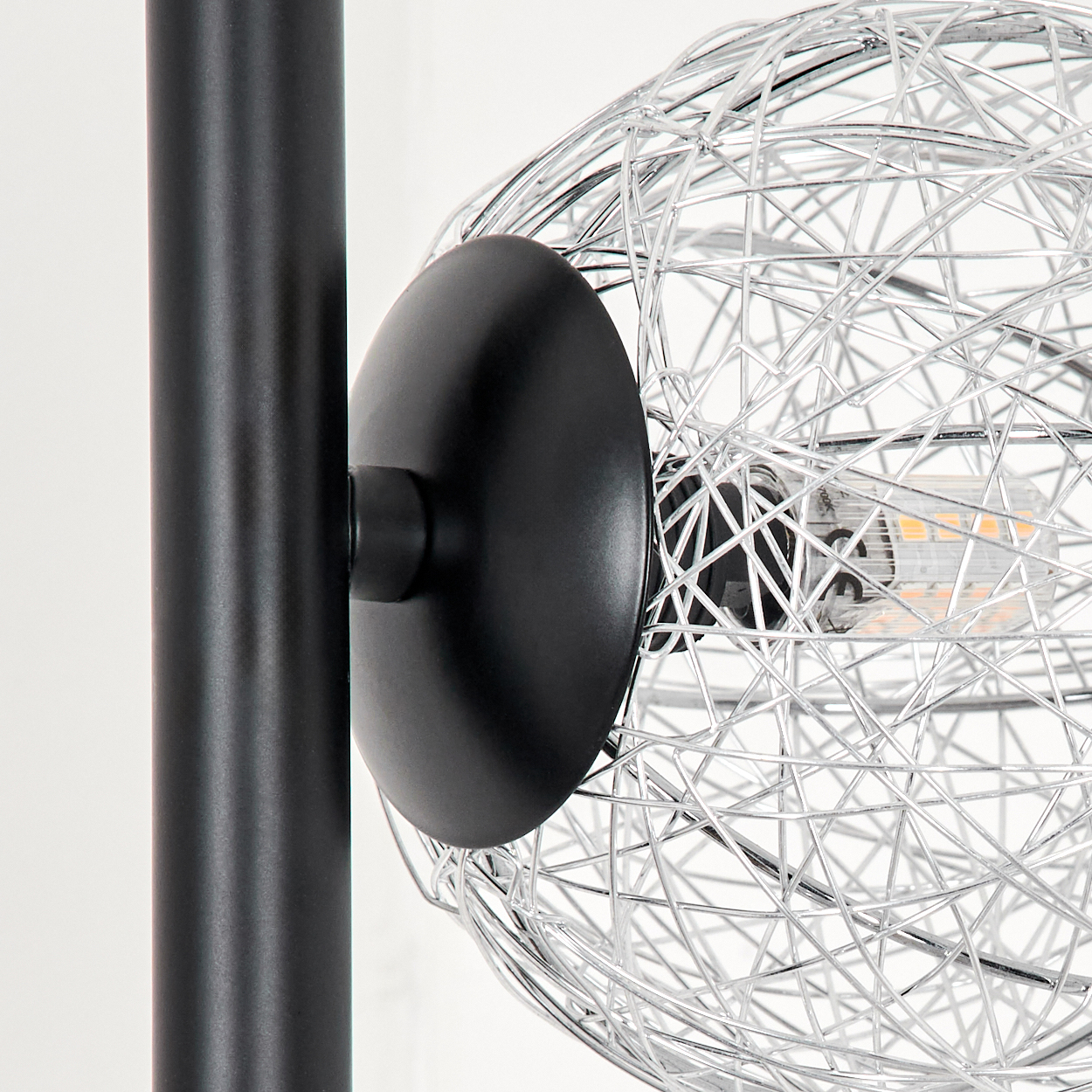Nahaufnahme einer Lampe mit schwarzem Pfosten, runder schwarzer Basis und silberner Drahtkugel. Der Hintergrund ist weiß.