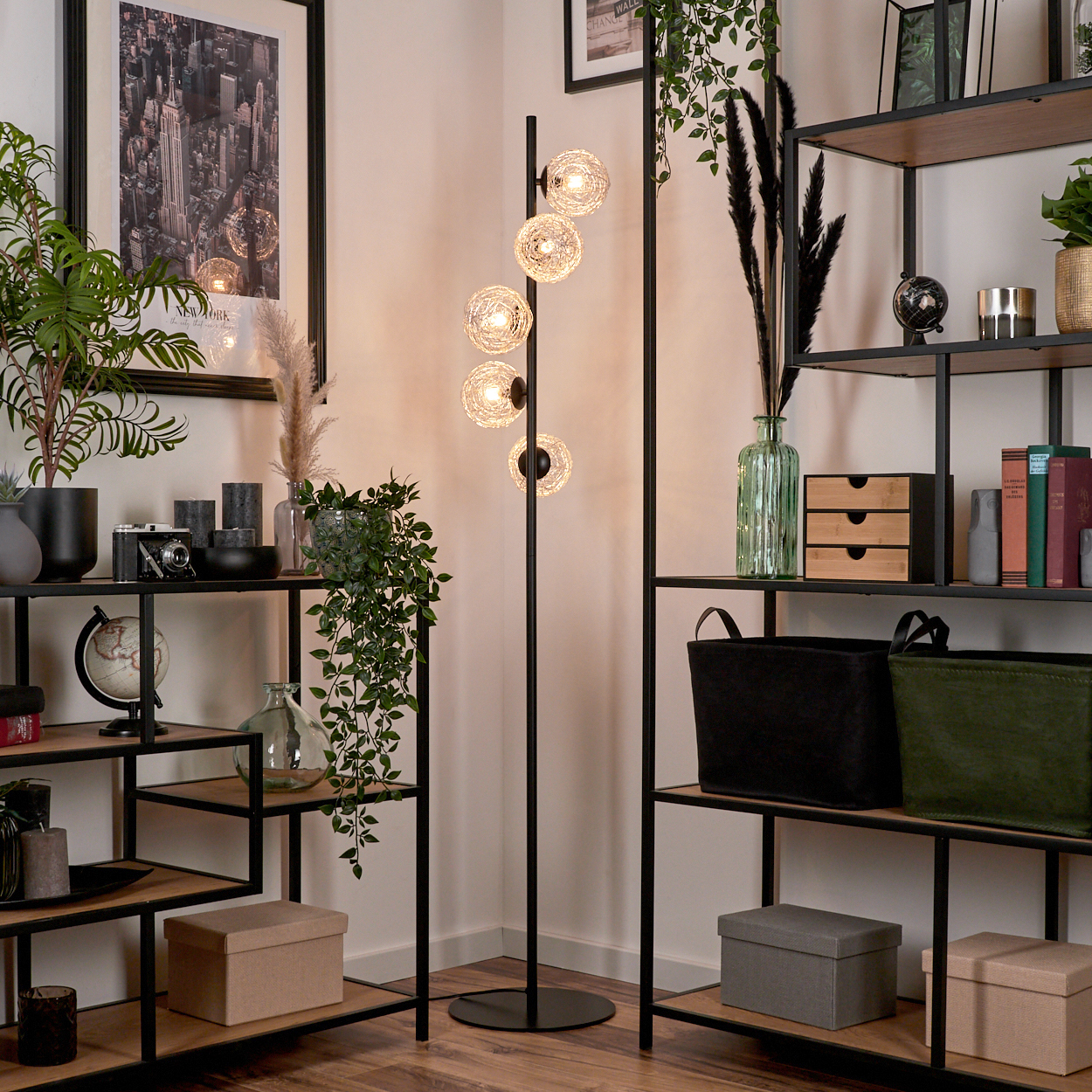 Wohnzimmer mit Stehlampe und Regalen. Die Lampe hat fünf Kugelleuchten. Regale enthalten Pflanzen, Bücher, Kisten und Dekorationsartikel.