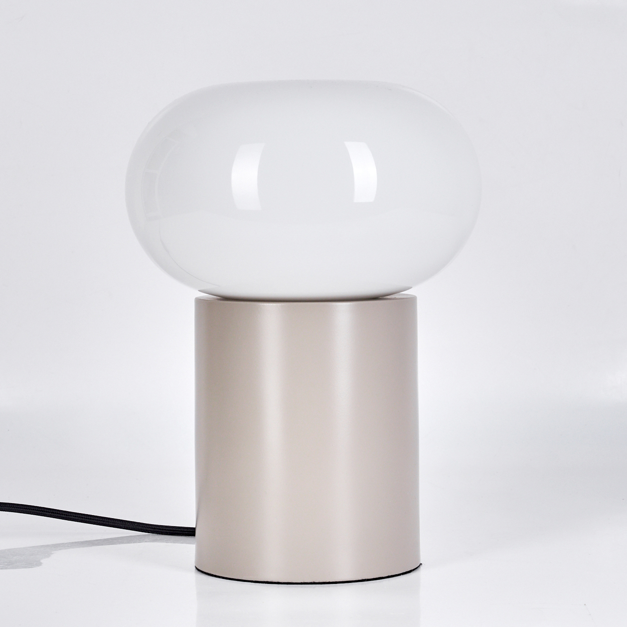 Eine moderne Tischlampe mit weißem, kugelförmigem Schirm auf einem zylindrischen, beigefarbenen Sockel. Ein schwarzes Netzkabel geht von der Basis aus.