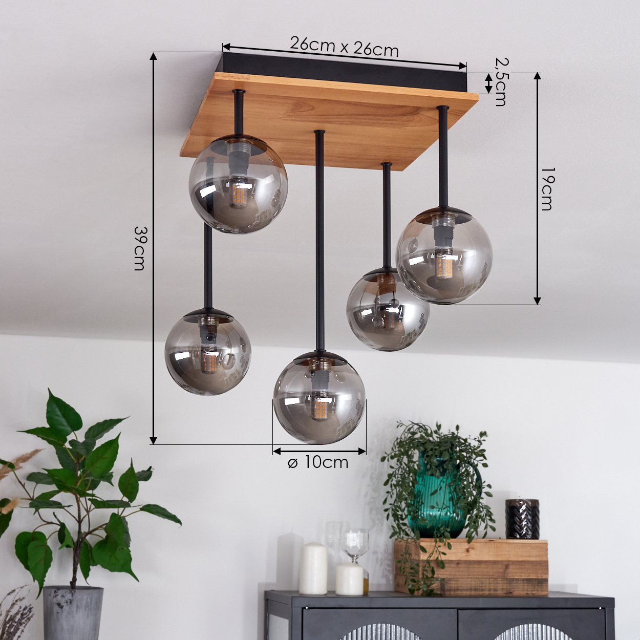 Eine moderne Leuchte mit fünf Glaskugel-Schirmen hängt an einem Holzquadrat. Pflanzen und Möbel sind im Hintergrund.